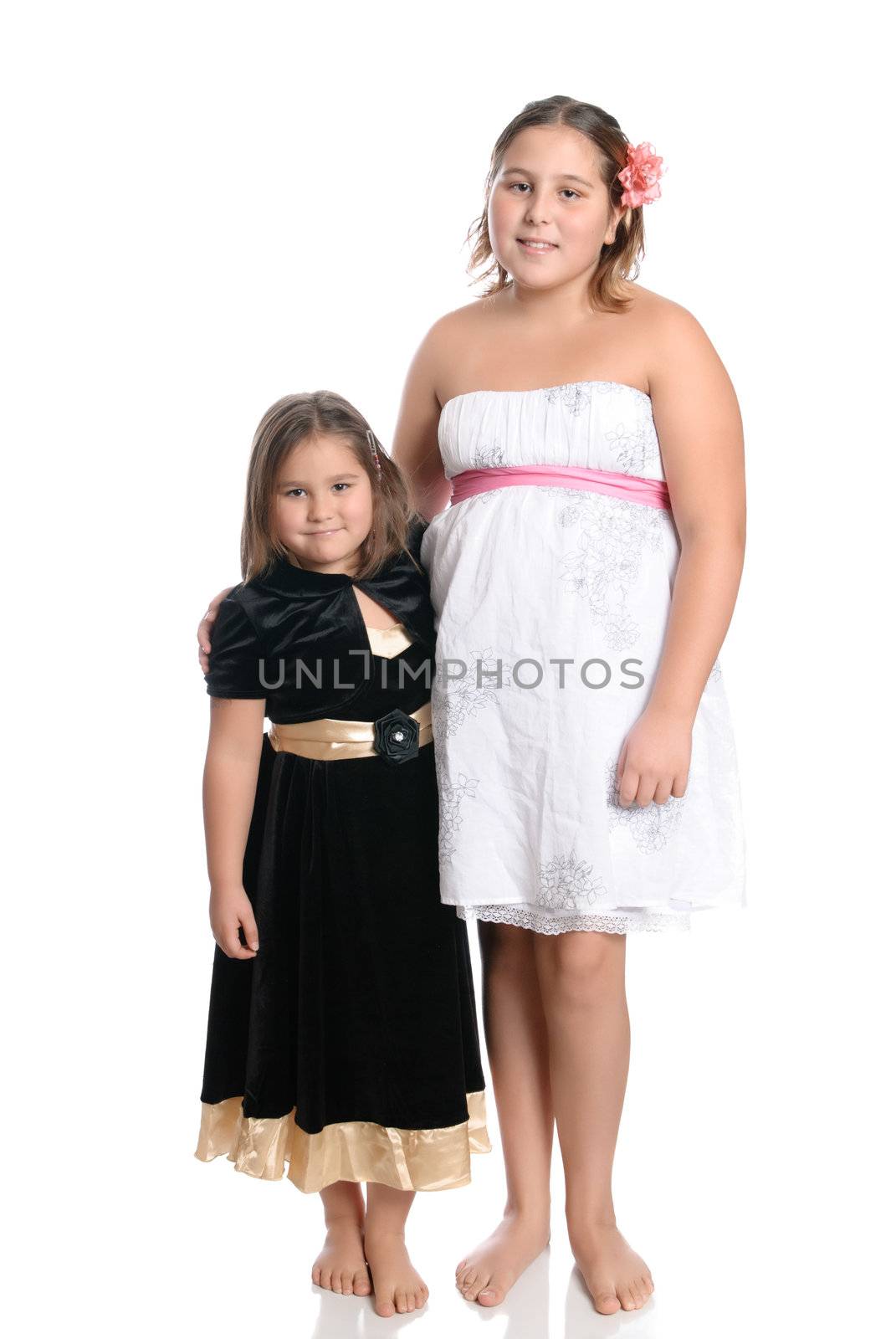 Two young sisters smiling and wearing pretty dresses are isolated on a white background.