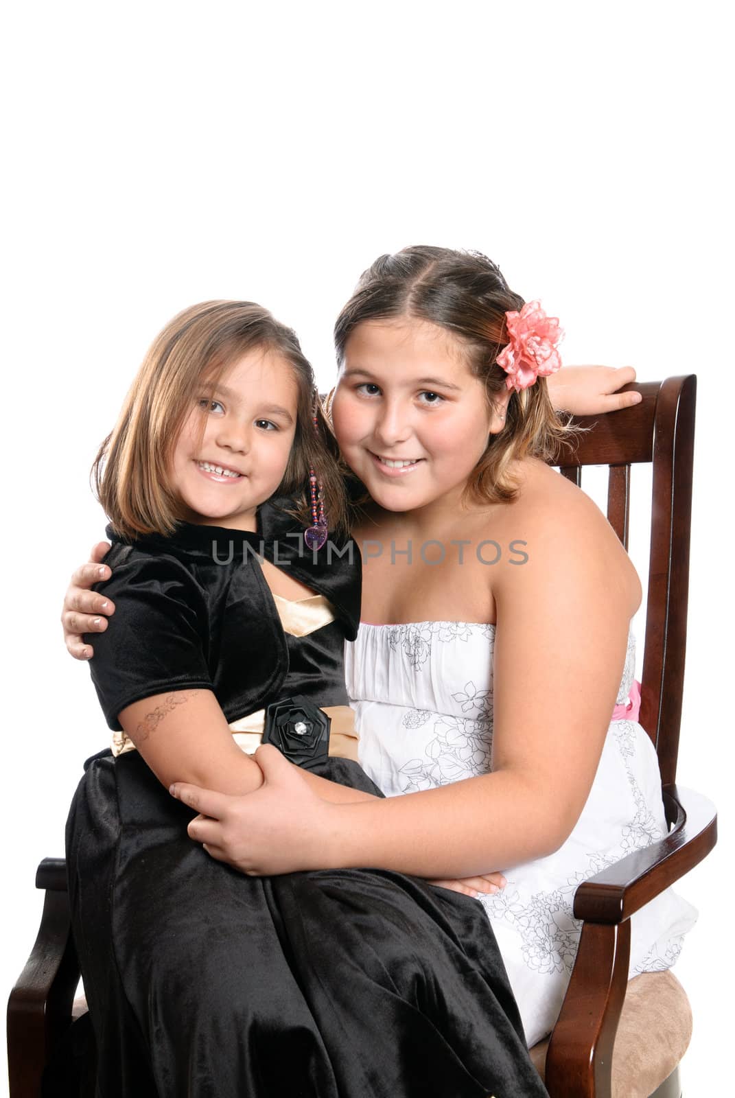 Two happy sisters are sitting on a wooden chair, isolated against a white background.