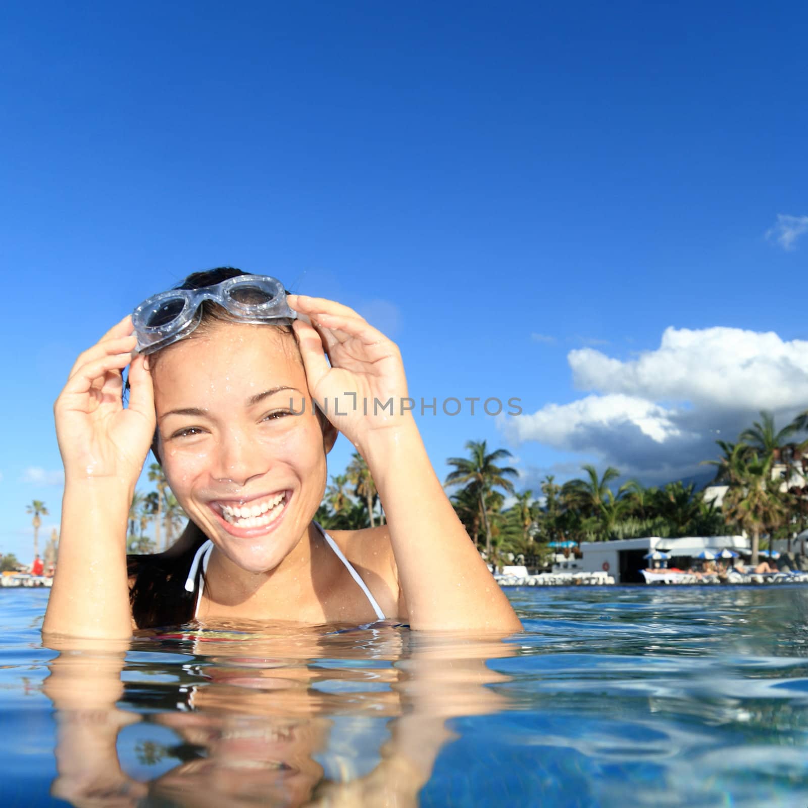 Woman smiling in swimming pool in luxury resort. Young smiling woman model with swimming goggles looking happy at camera.