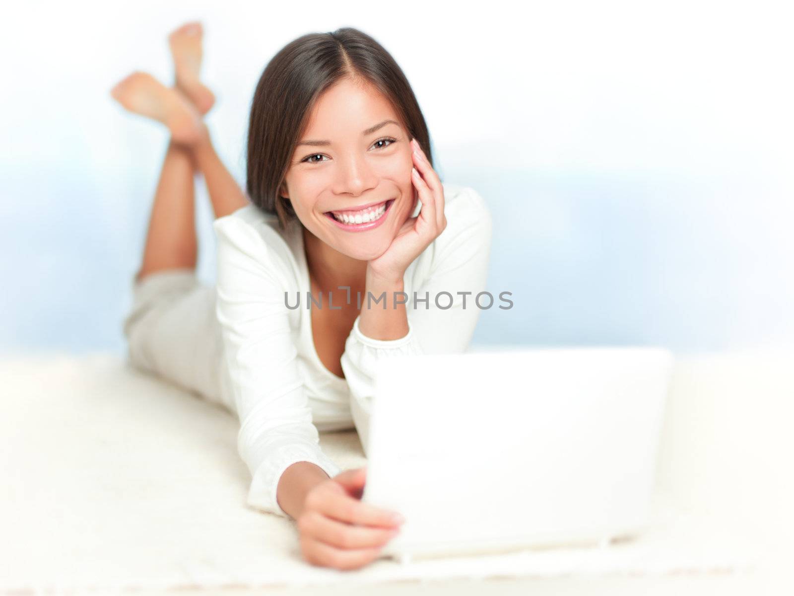 Portrait of smiling woman using laptop lying on the floor with window showing ocean view background. Beautiful female model
