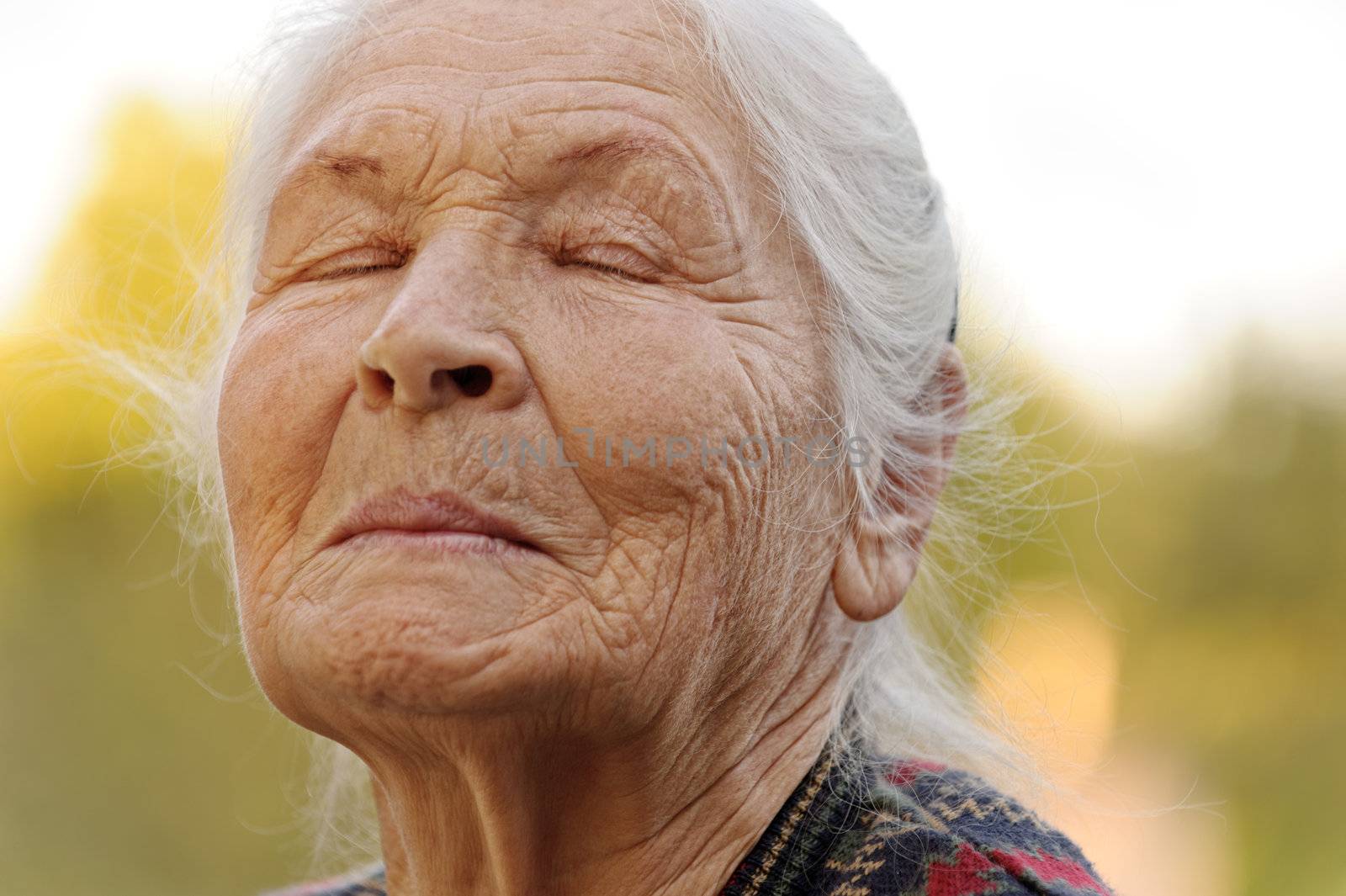 The elderly woman with closed eyes. A photo outdoors