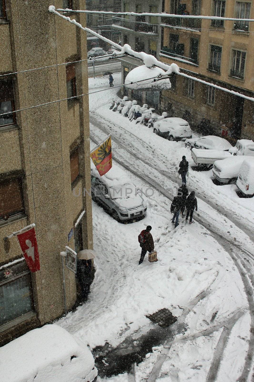 Walkers in the street with cars covered with snow by snowing and cold weather, Geneva, Switzerland