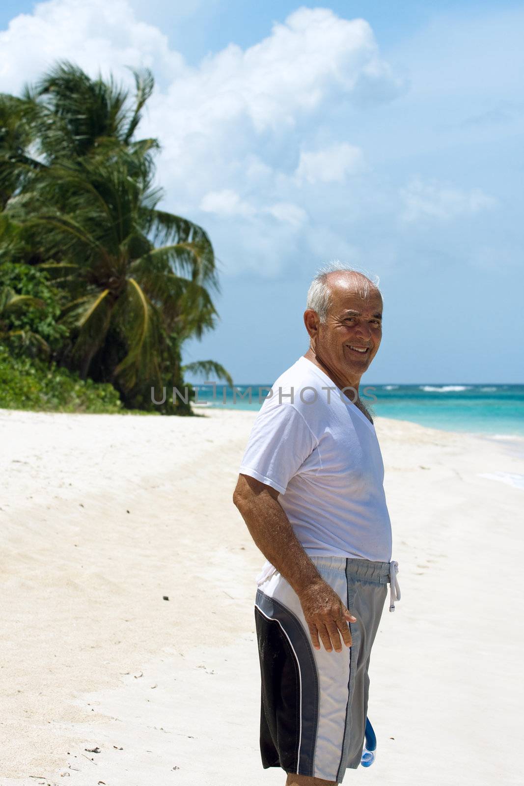 A older Hispanic senior citizen man standing on a tropical beach in the Caribbean.