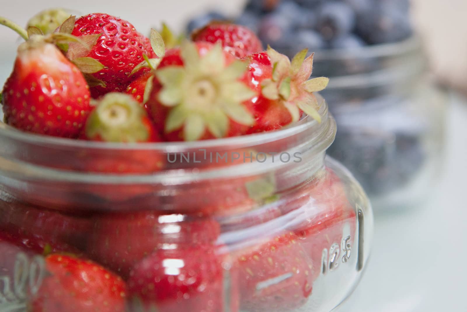 Bunch of fresh, red Strawberries with blueberry jar in the background