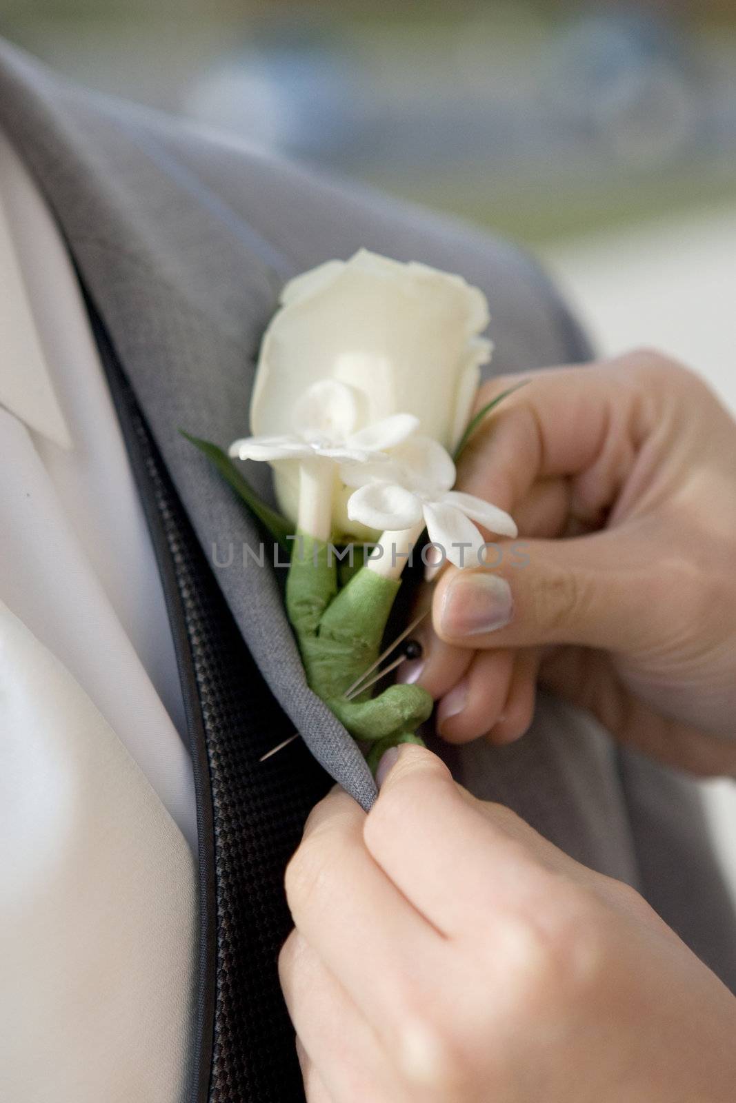 Woman attaching a white bouttonniere to man's gray suit