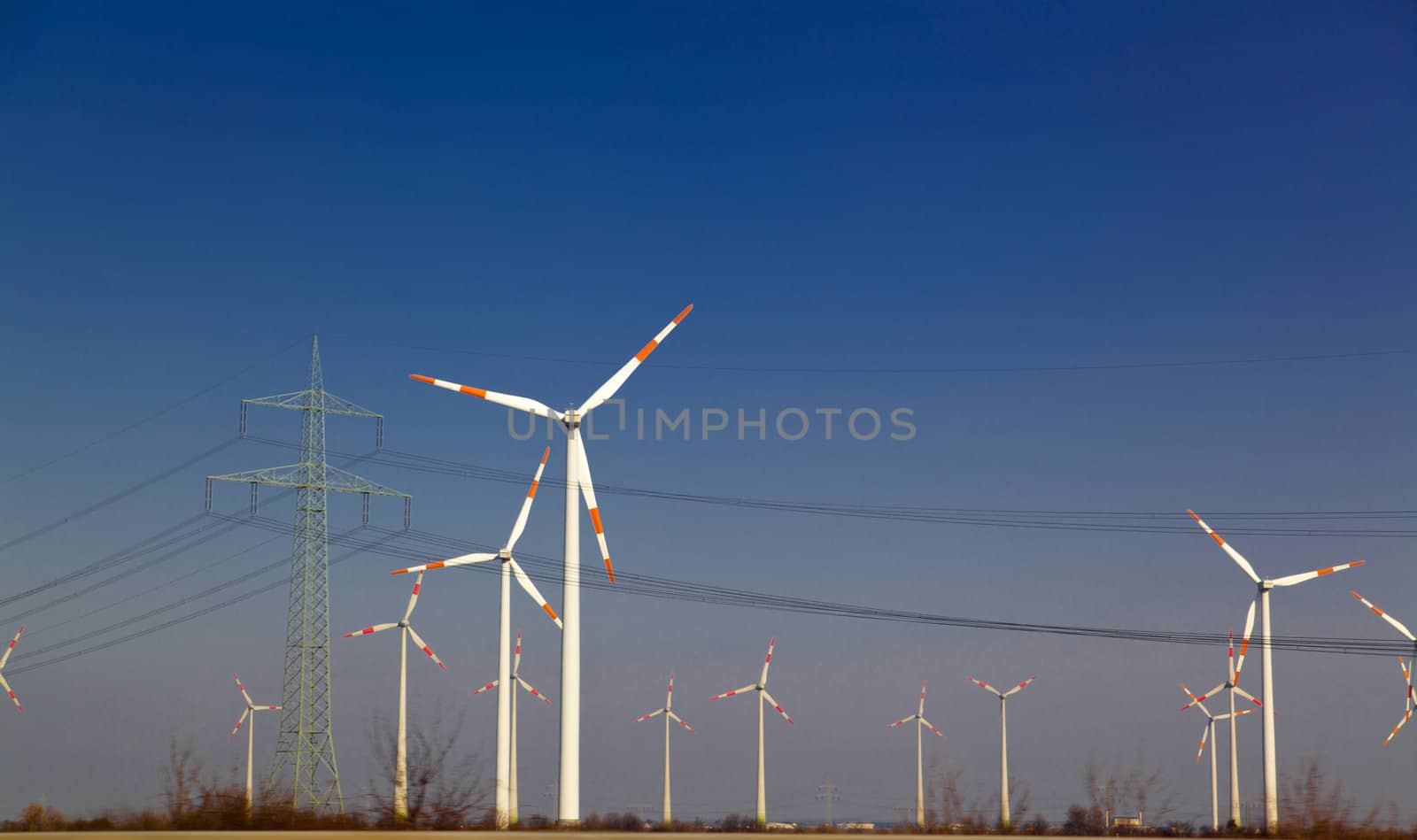Wind turbine and power lines against blue sky

