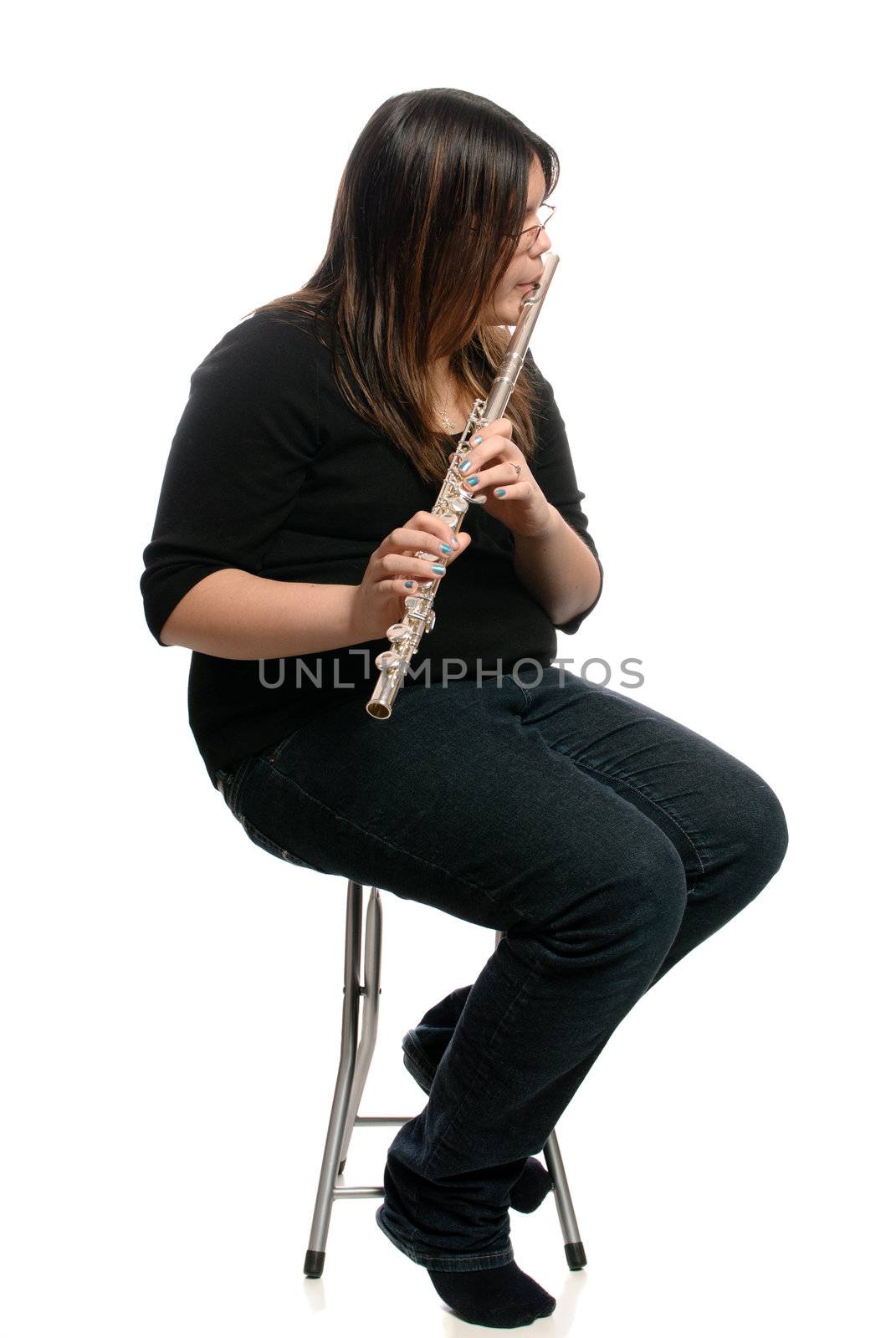 A teenage girl is sitting on a stool while playing the flute, isolated against a white background.