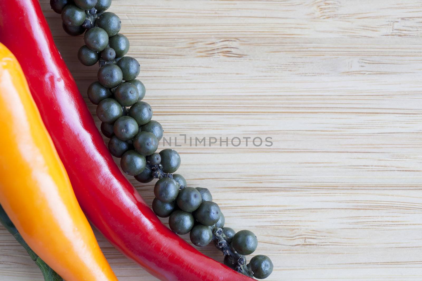 Red and orange hot peppers and fresh on the stalk pepper corns on wooden surface with copy space.