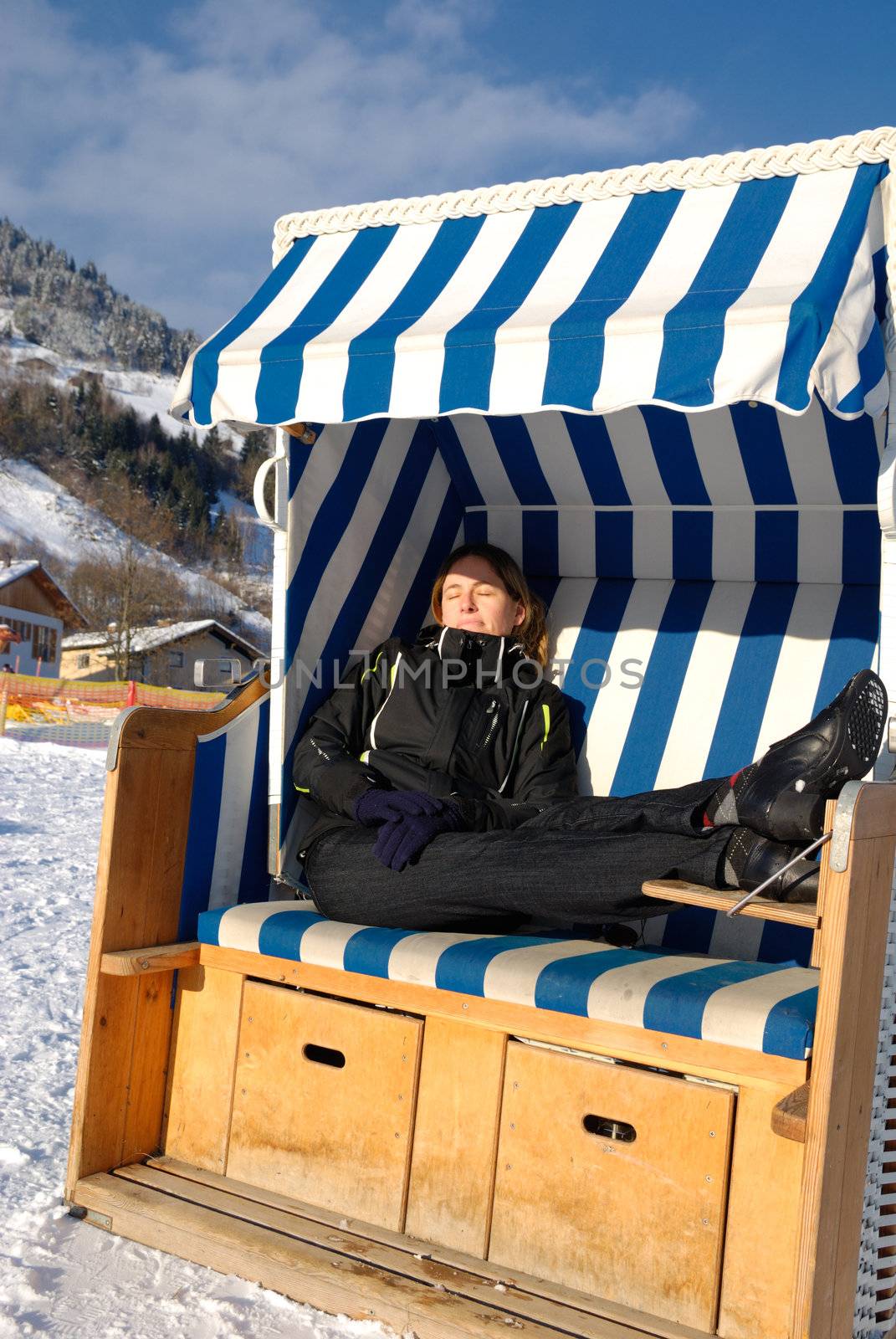 Young woman sleeping in roofed wicker beach chair on a sunny winter day in austria.