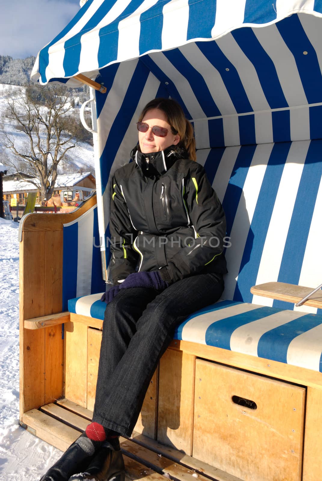 Young woman relaxing in roofed wicker beach chair on a sunny winter day in austria.