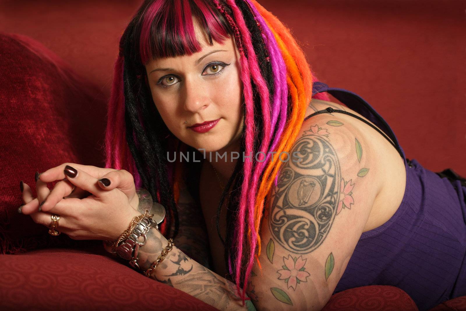 Portrait of a beautiful female goth with dreadlocks on a red couch.
