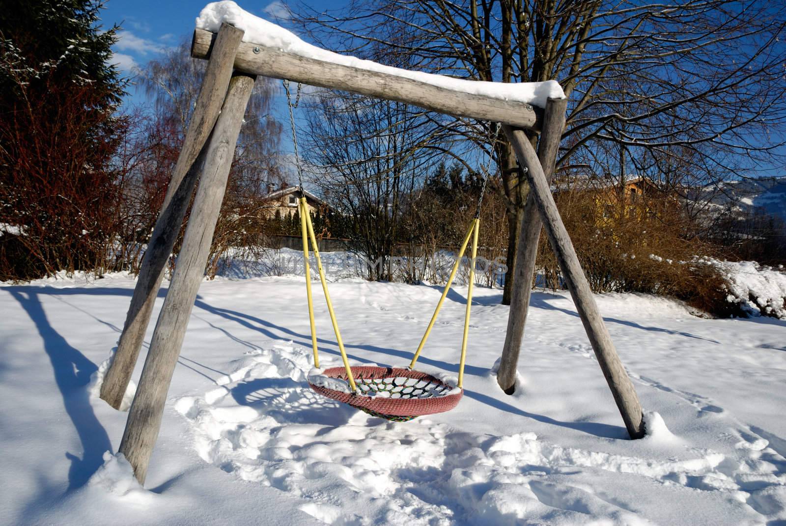 Snow covered swing at empty playground in winter.