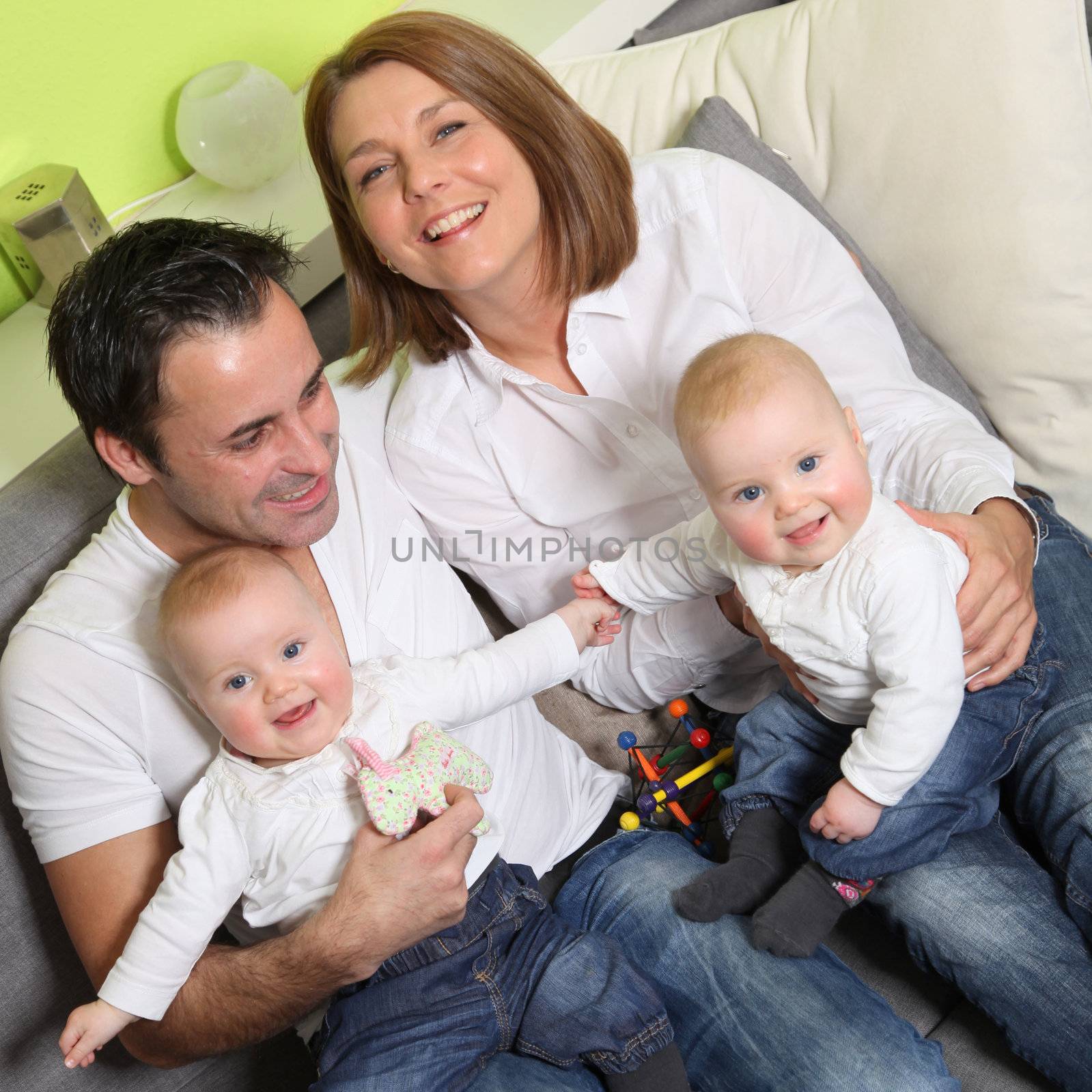 Young, happy family with two children and babies - twins at home on the couch and have fun with the kids.

