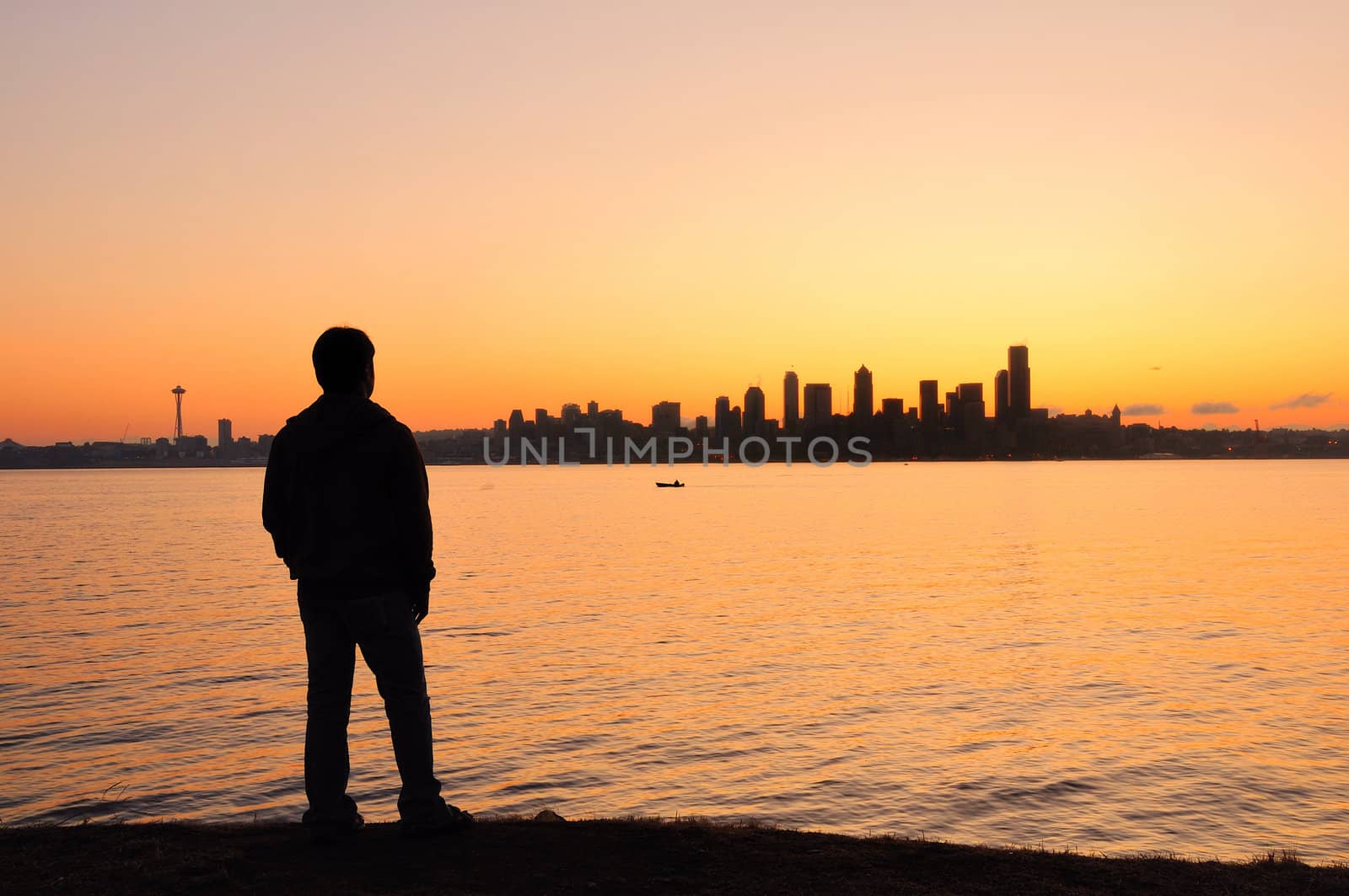 A young man watching the sun rise behing the Seattle skyline across the bay