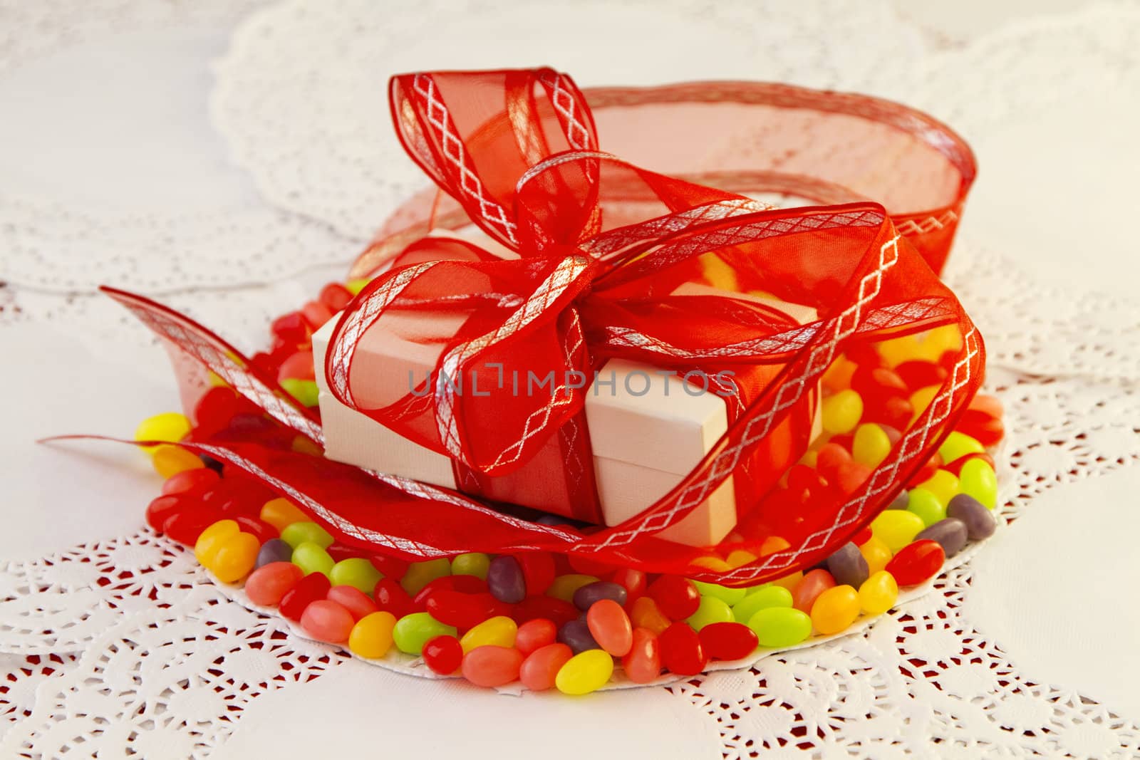 White package wrapped in red ribbon placed on colorful jellybeans and paper doilies