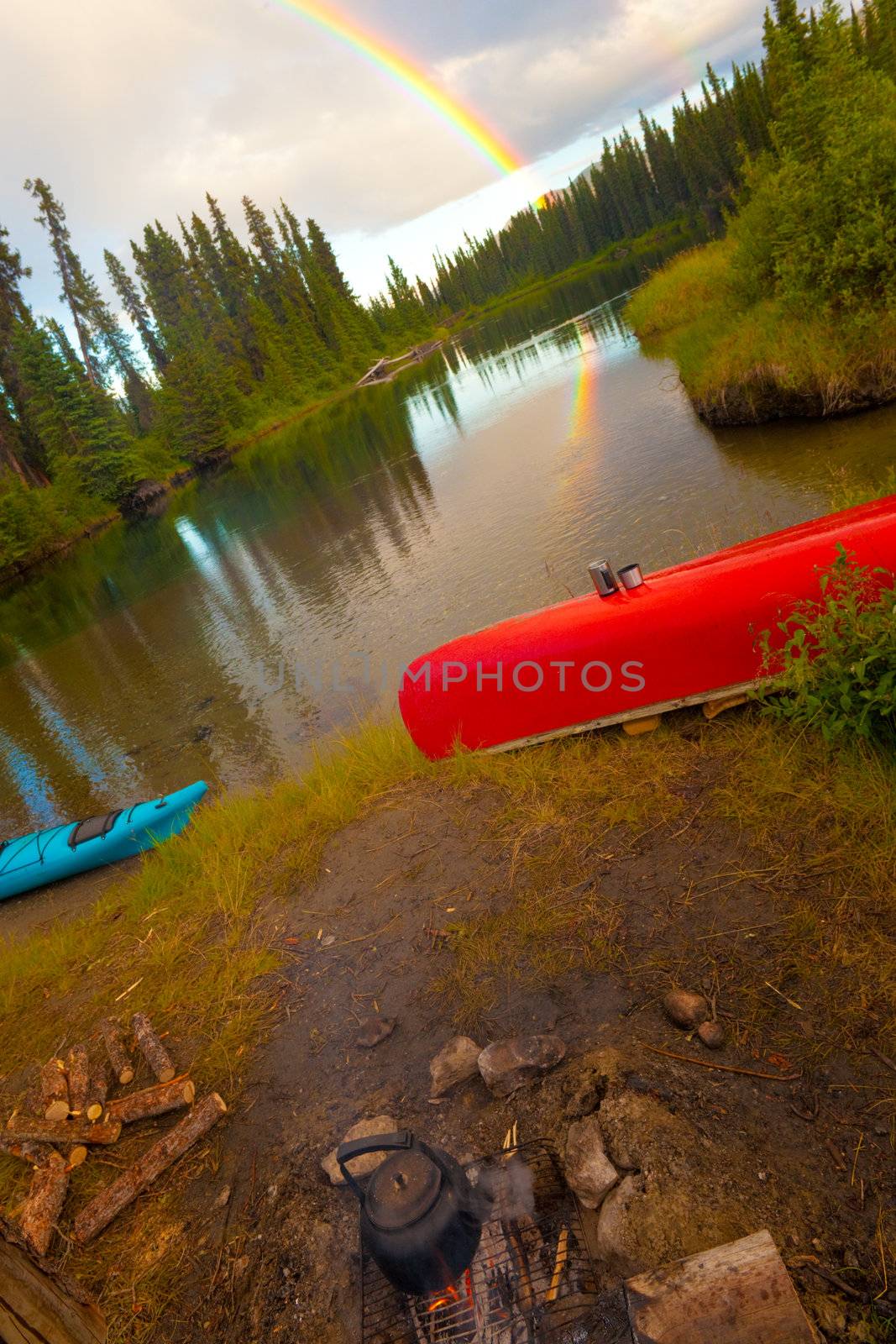 Overturned canoe and campfire under bright rainbow