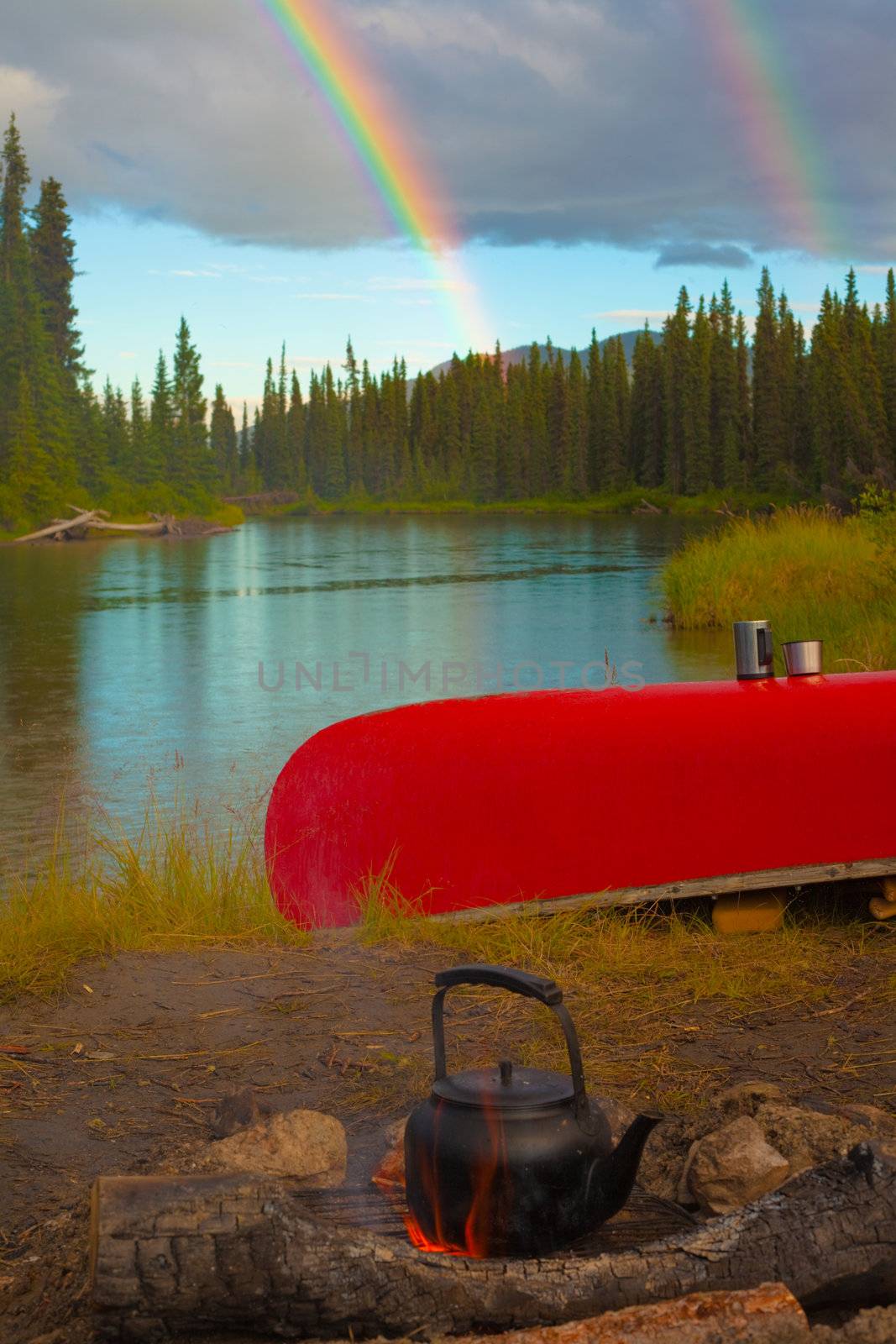 Overturned canoe and campfire under bright rainbow