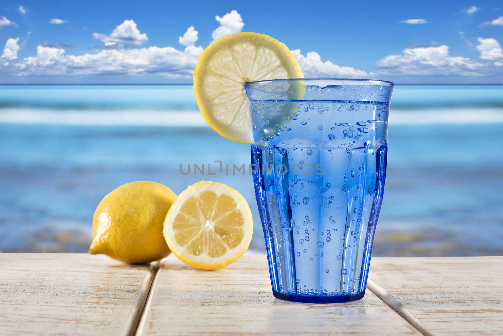 a Blue glass with sparkling water and lemon on a wooden deck overlooking a tropical beach