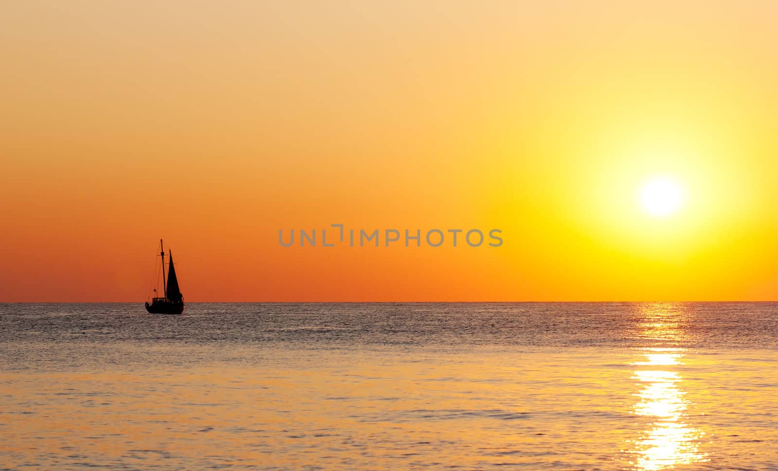 Golden sunset on a sea with silhouette of a yacht.