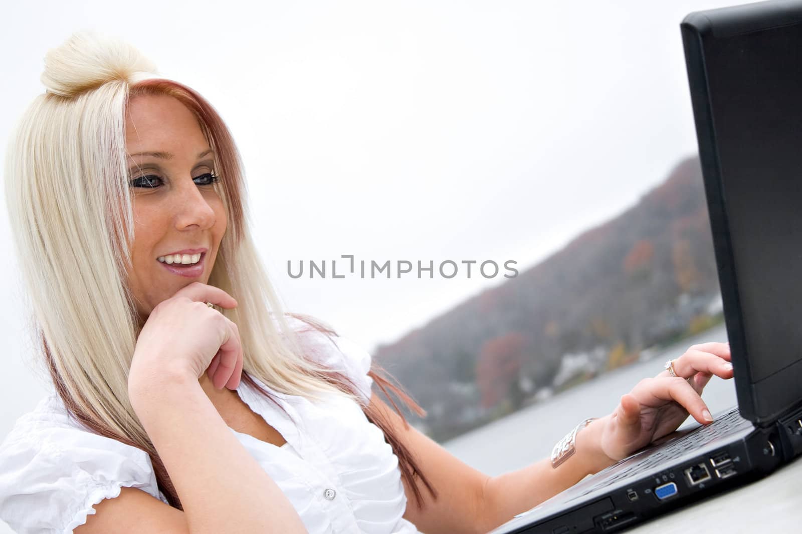 A beautiful young blonde business woman outdoors with her laptop looks at the screen with a smile on her face.