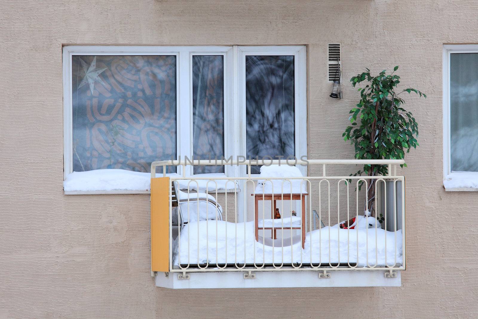 balcony of an apartment building is kneedeep covered with snow - snowy table, chair and plant on the balcony