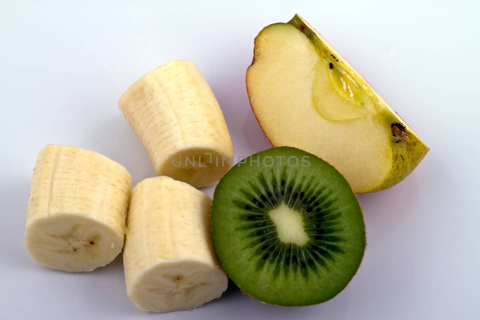 Banana, kiwi and apple pieces on reflecting white surface