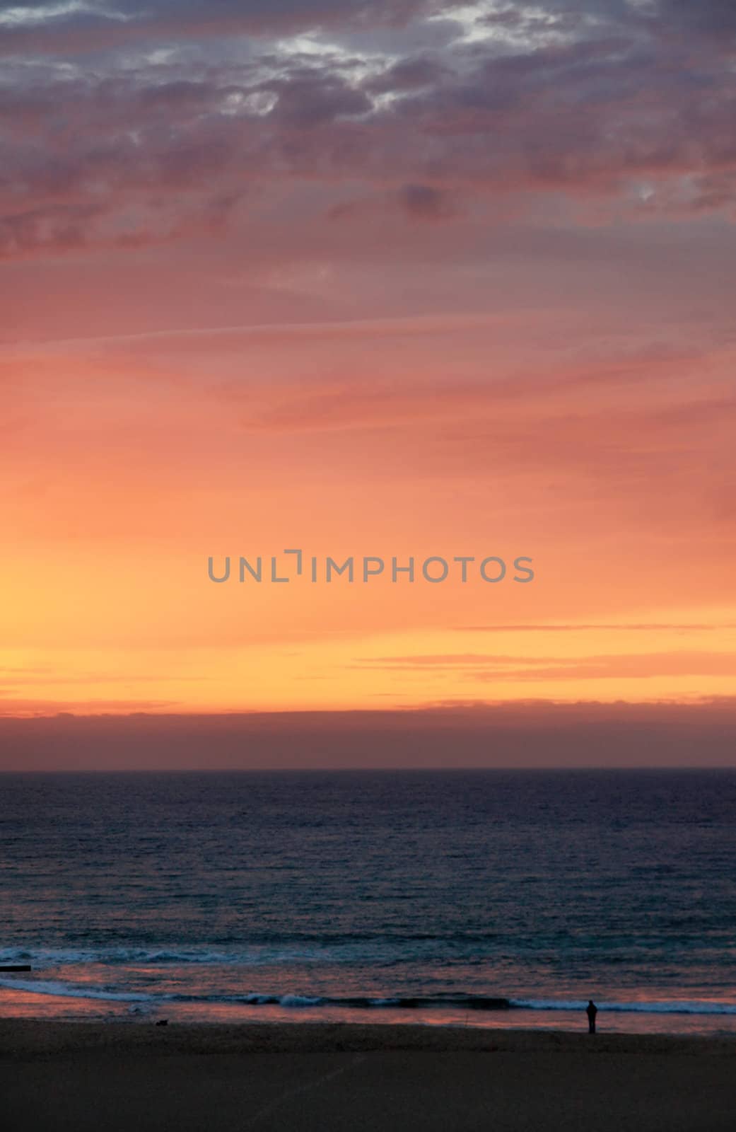 view of a lonely figure on the shore of a beach at sunset.