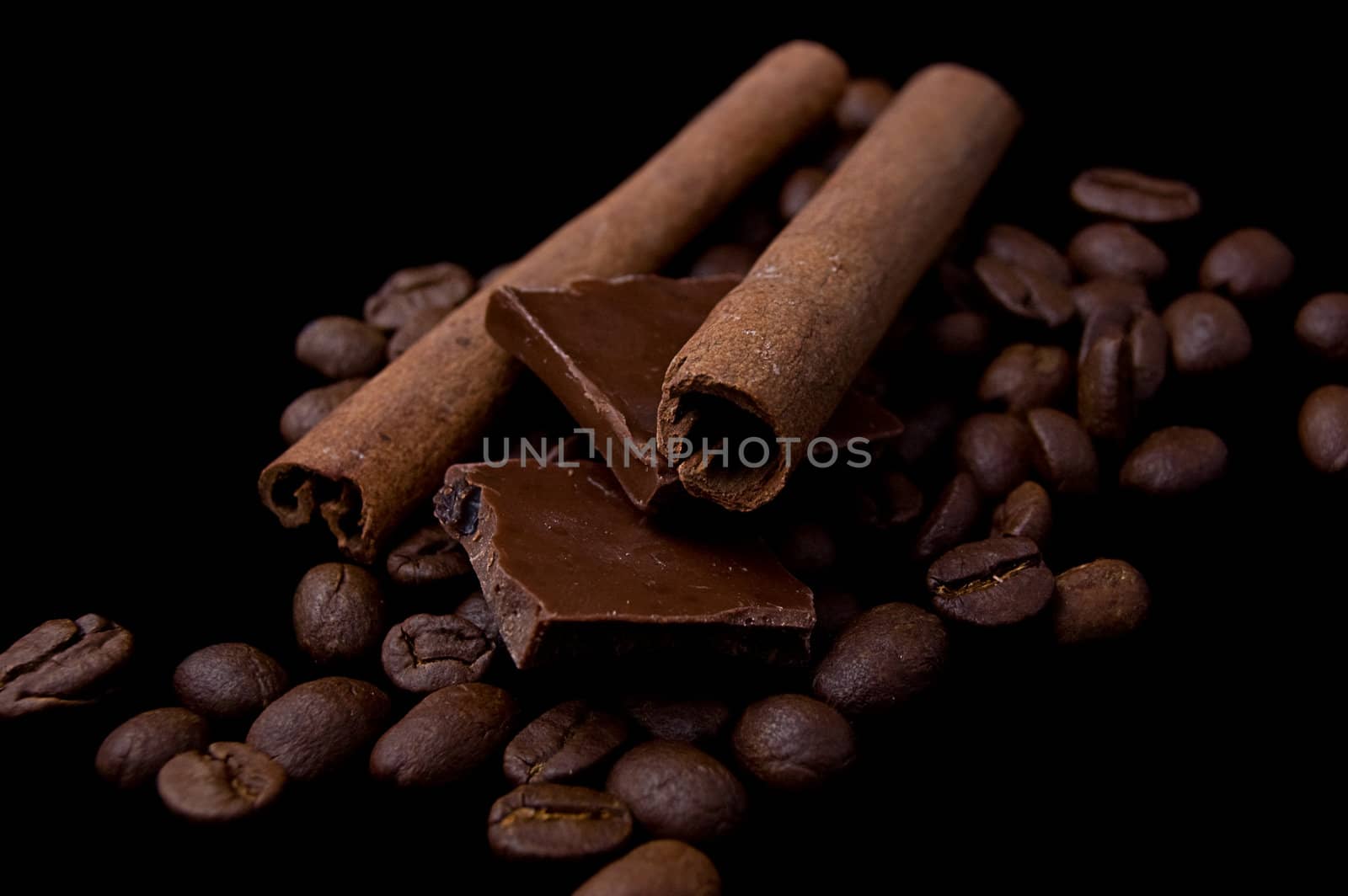 Cinnamon sticks over coffee beans and chocolate on black
