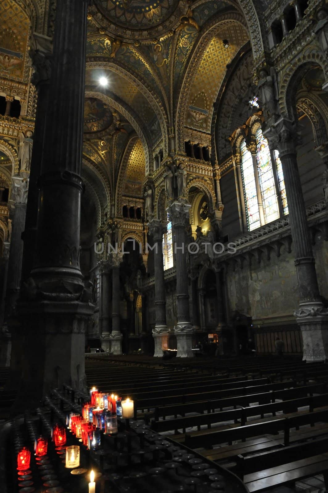 Church interior with big archs, lot of gilding and some candles on a support