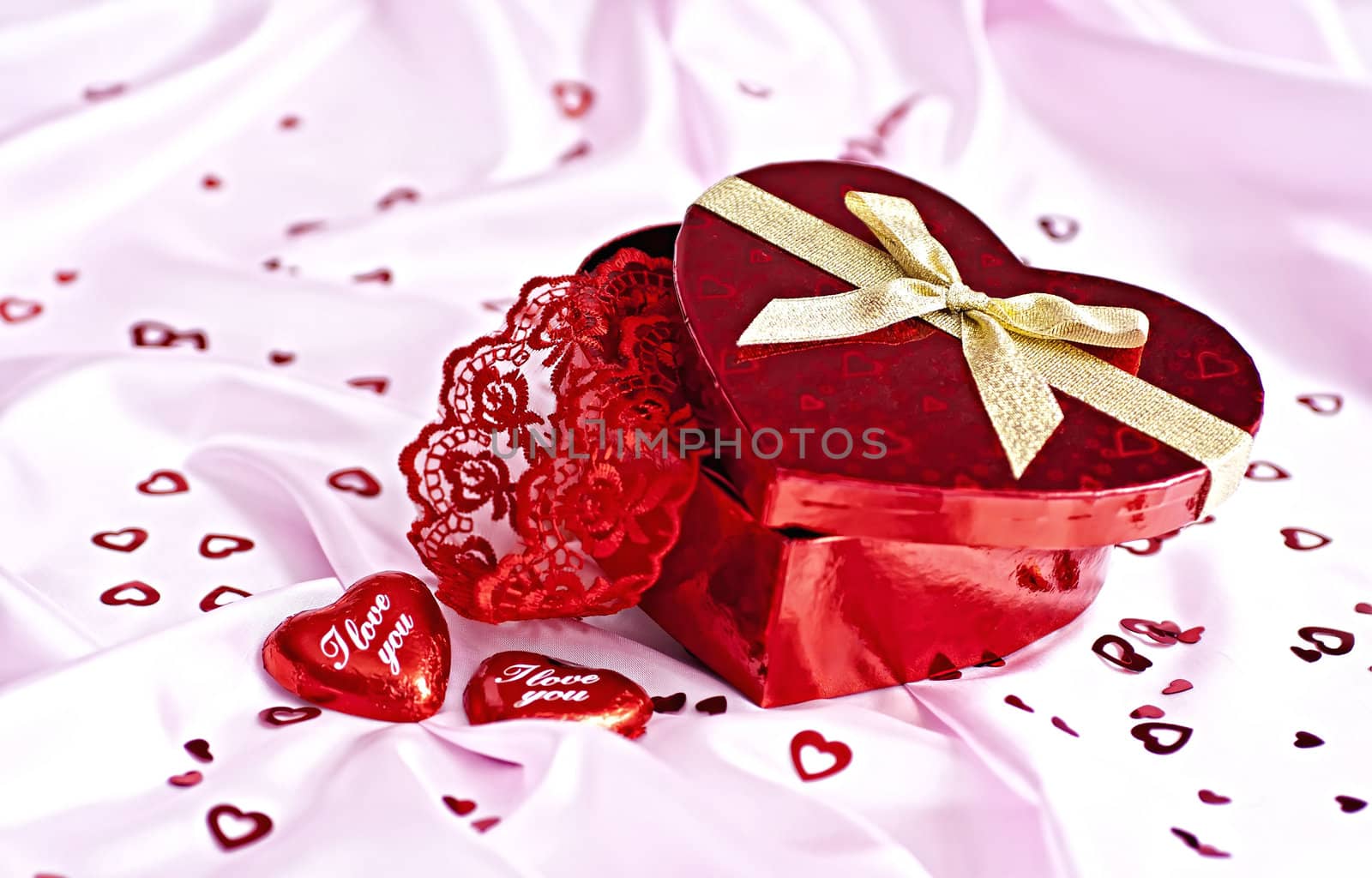 Pink bedding, gift box heart-shaped chocolate candy with the words I Love You and a lot of small distributed hearts. Surprise to the woman.
