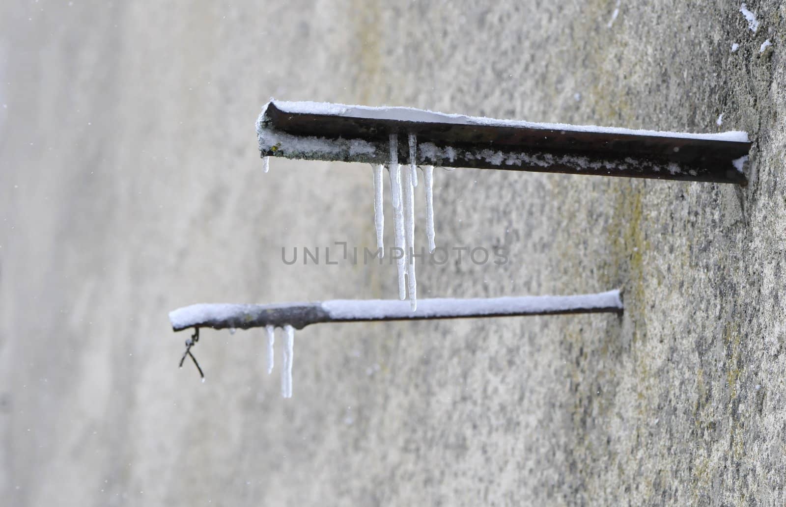 Ice stalactites on rusted bars hammered in an old wall