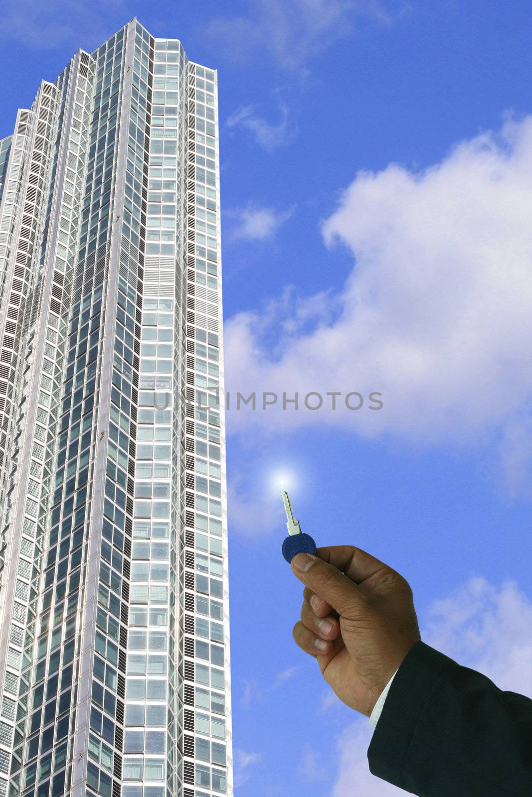 Businessman holding key,concept for real property,just sold,sales,new occupant- in a clear blue sky and high rise tower background.
