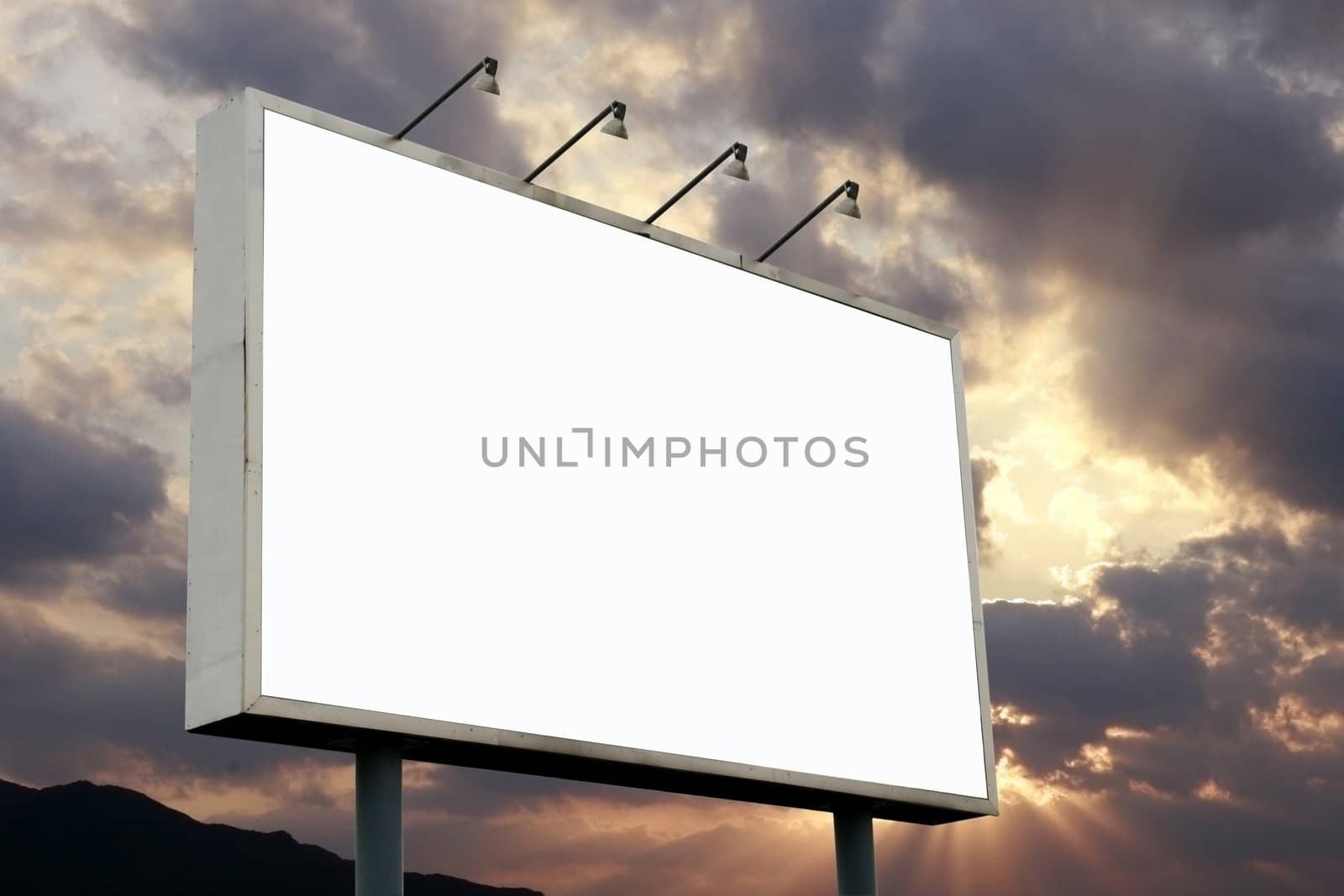 Blank Billboard at a dramatic sunset - sun rays in a horizon accentuates at dark clouds, noticeable is the rays on the clouds