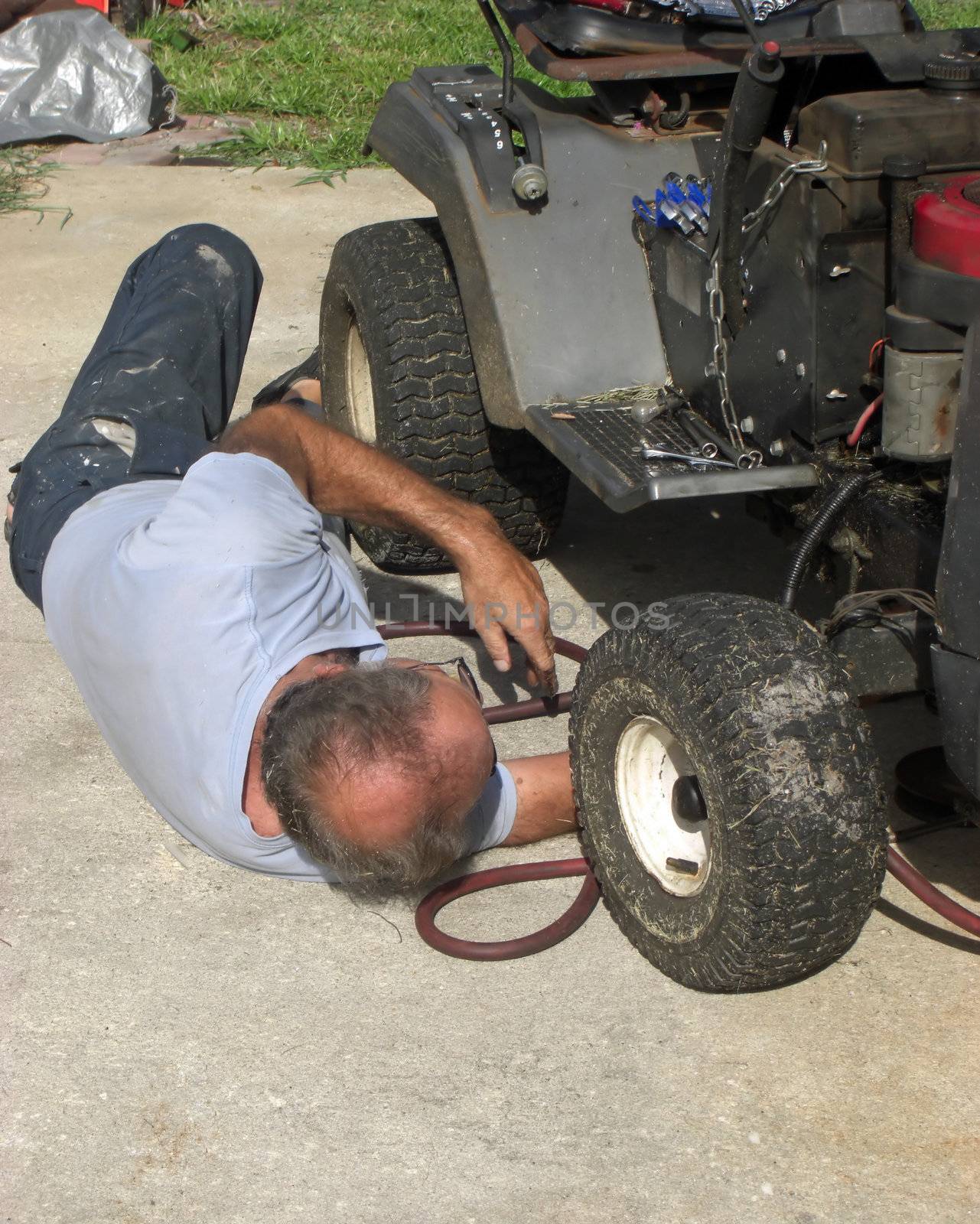 A man is lying on the ground and he is fixing an old lawn mower.
