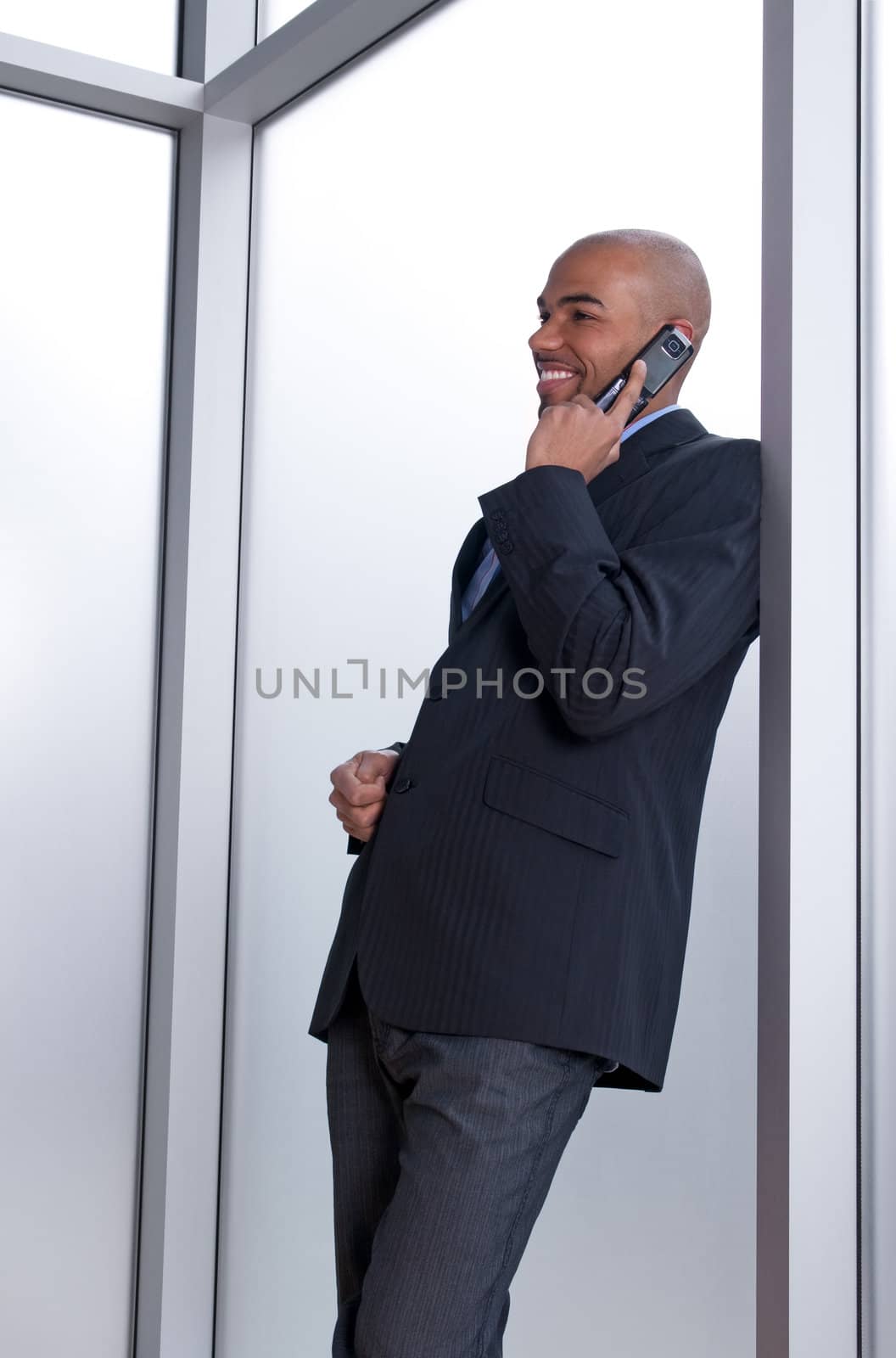 Businessman leaning against the window, talking on the phone and smiling.