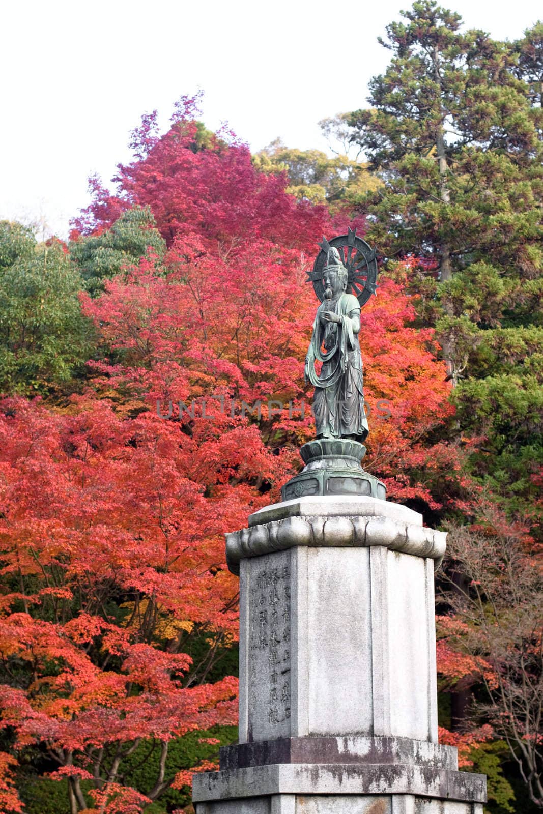 A statue ans red and green trees in a Japanese autumn park 
