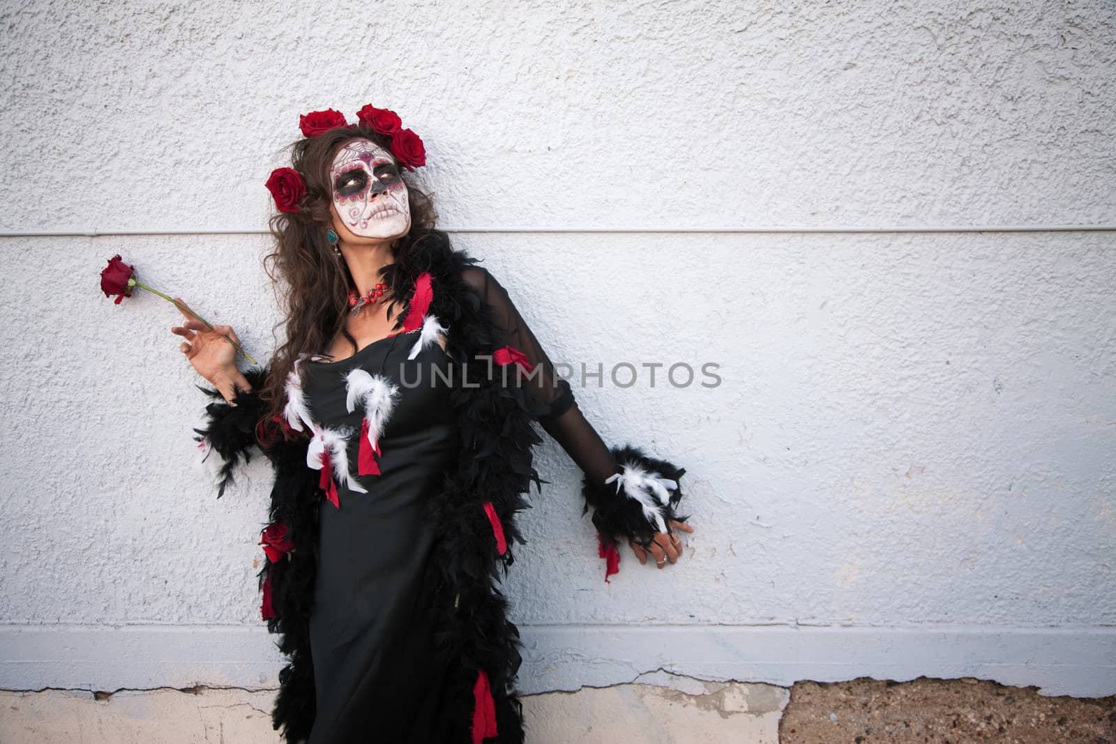 Woman in makeup for All Souls Day stands alongside a wall with red roses