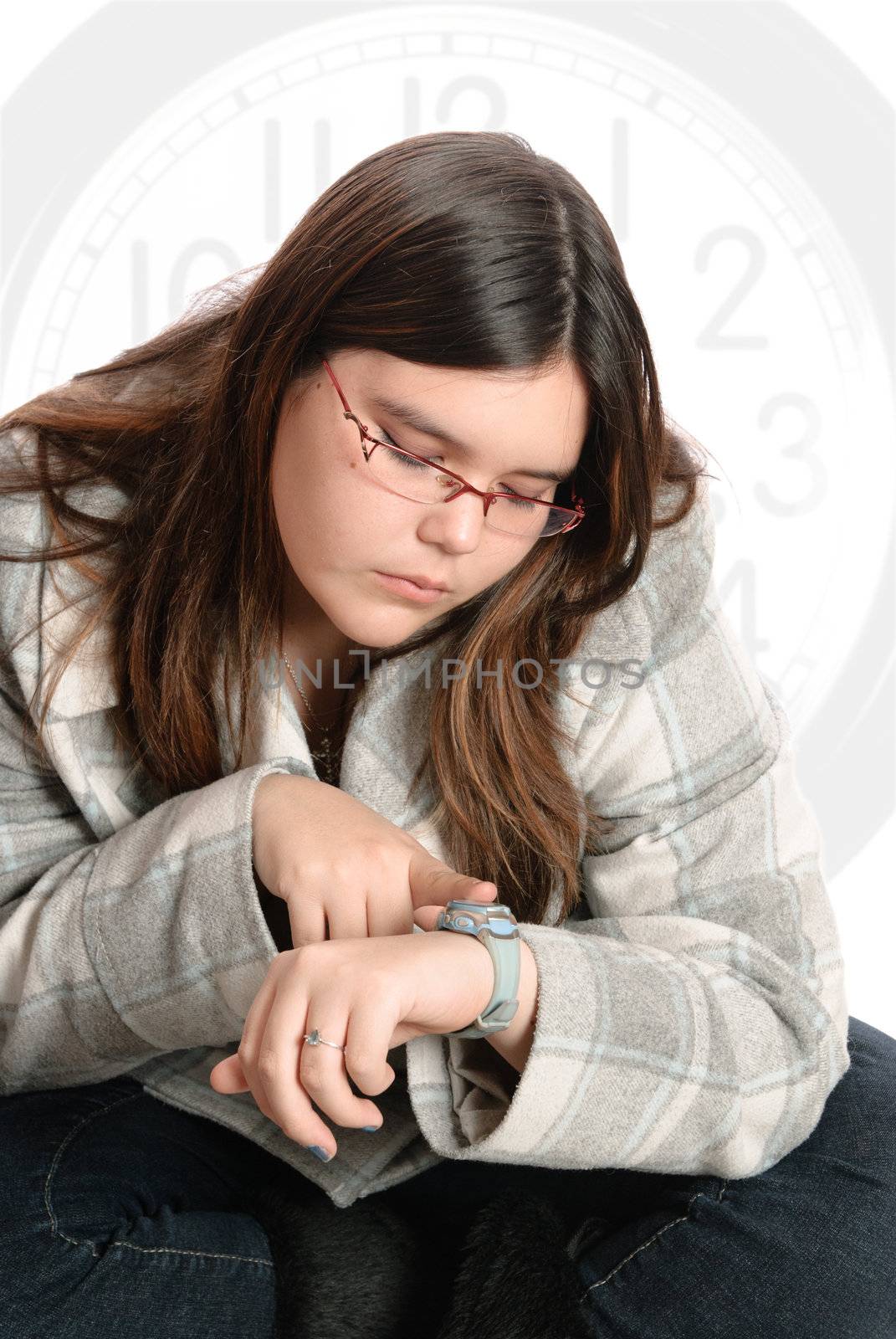 A young teenage girl is sitting with her legs crossed looking at her watch, waiting for something.