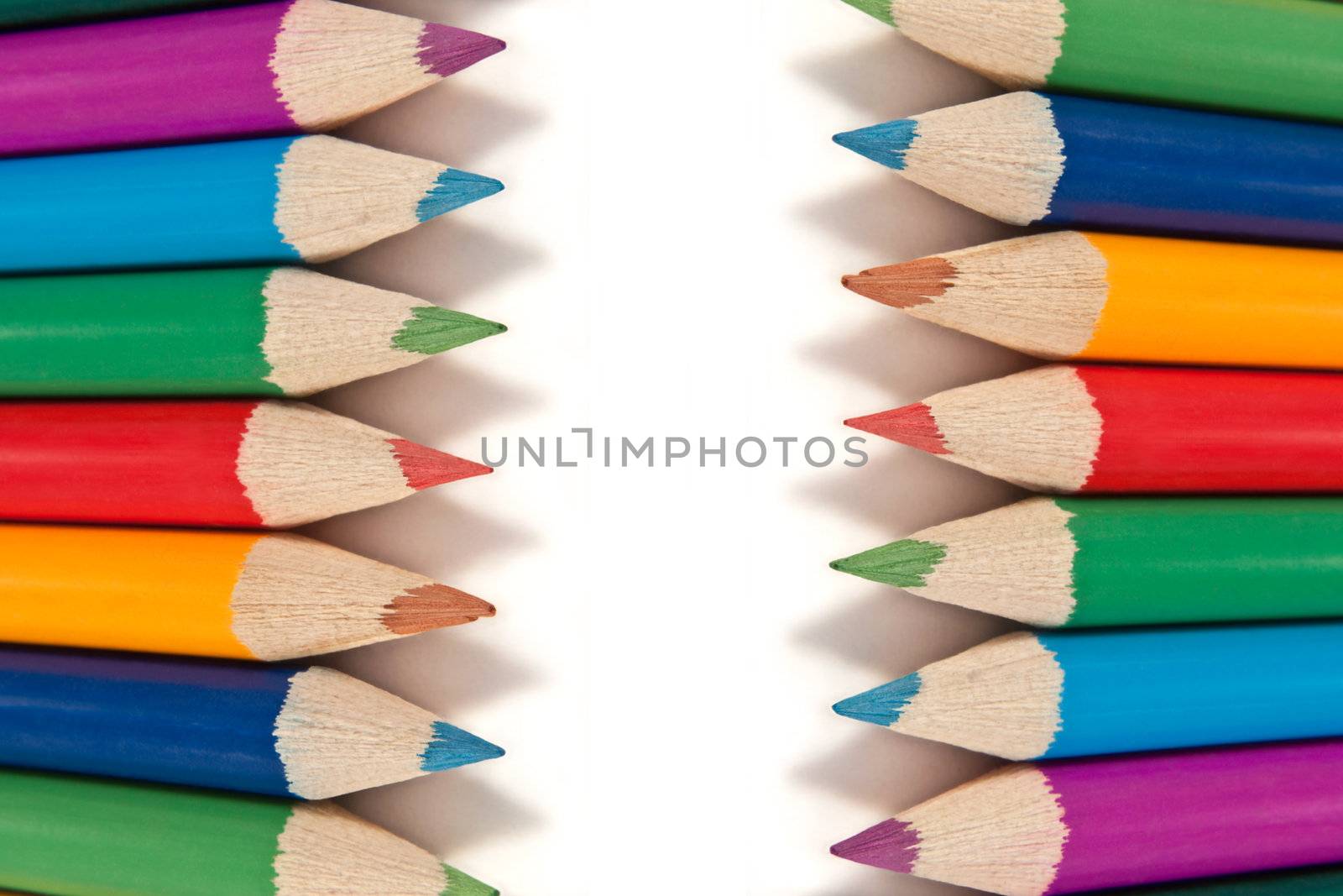 Close up capturing a selection of coloured artist pencils in arranged in a regular format over white.