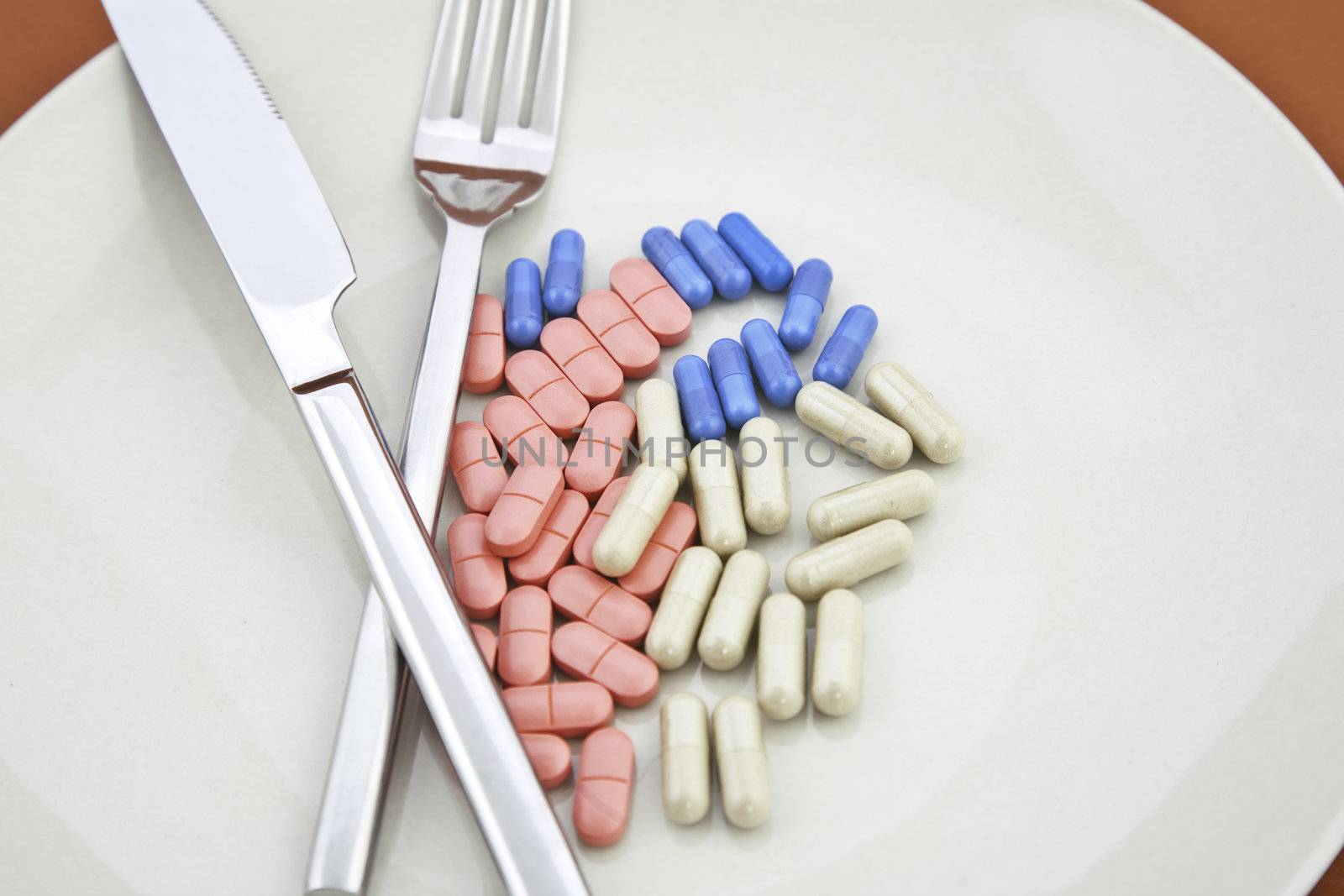 Vitamin pills and capsules on plate with knife and fork, a meal of pills