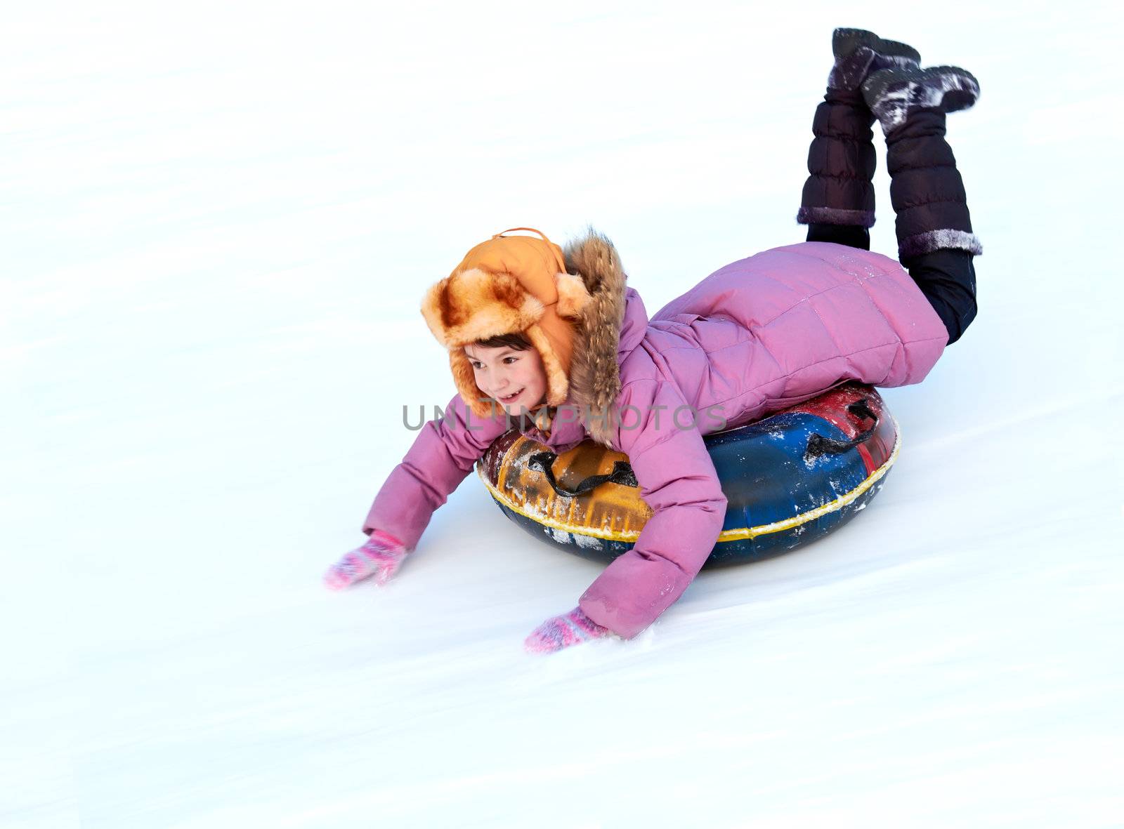 child riding color covered inner tube down snow cover hill at speed