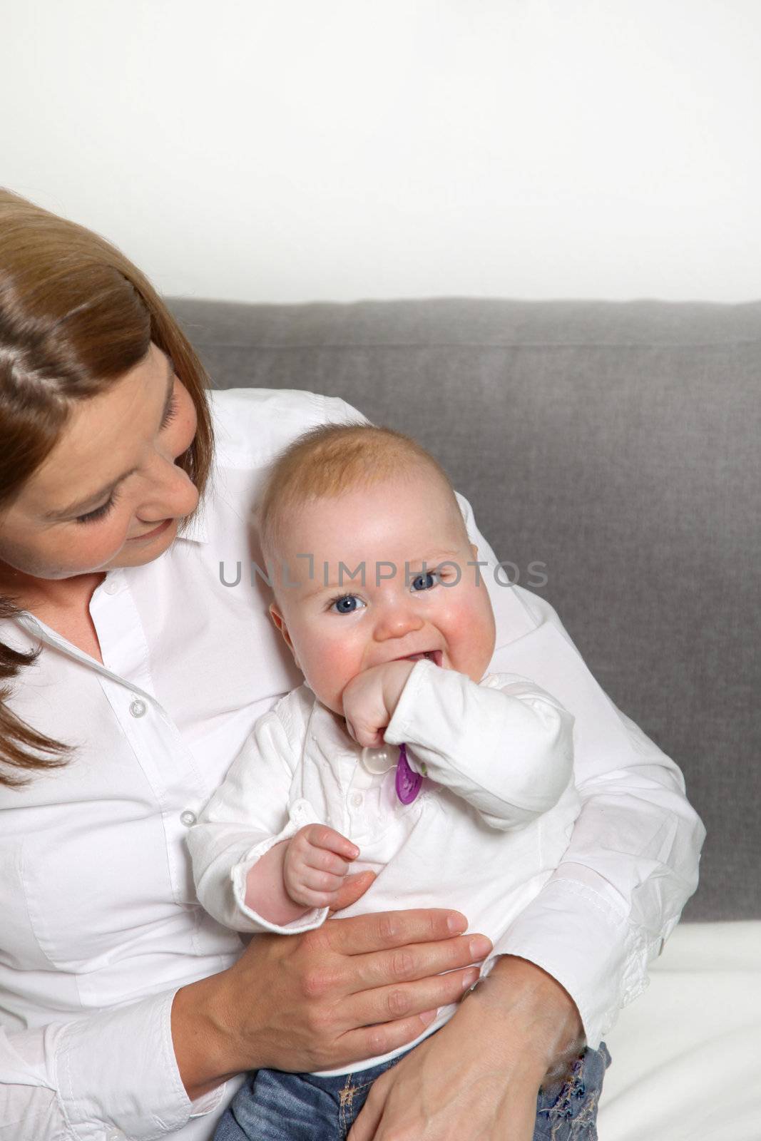 Smiling mother holding her baby. The baby sits on her leg and smiles toward the camera.
