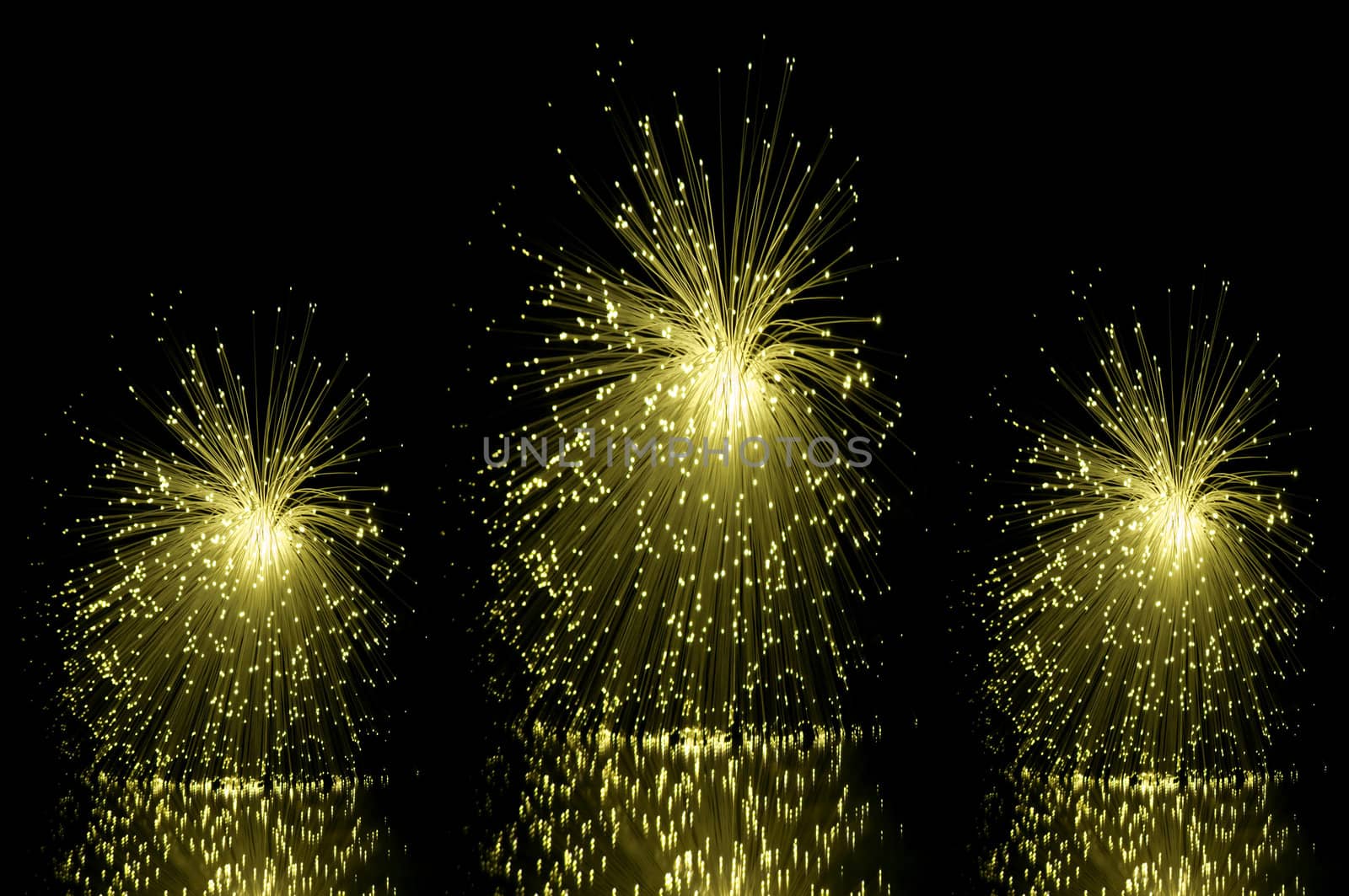 Low level angle capturing three yellow groups of illuminated fibre optic light strands against a black background and reflecting into the foreground.