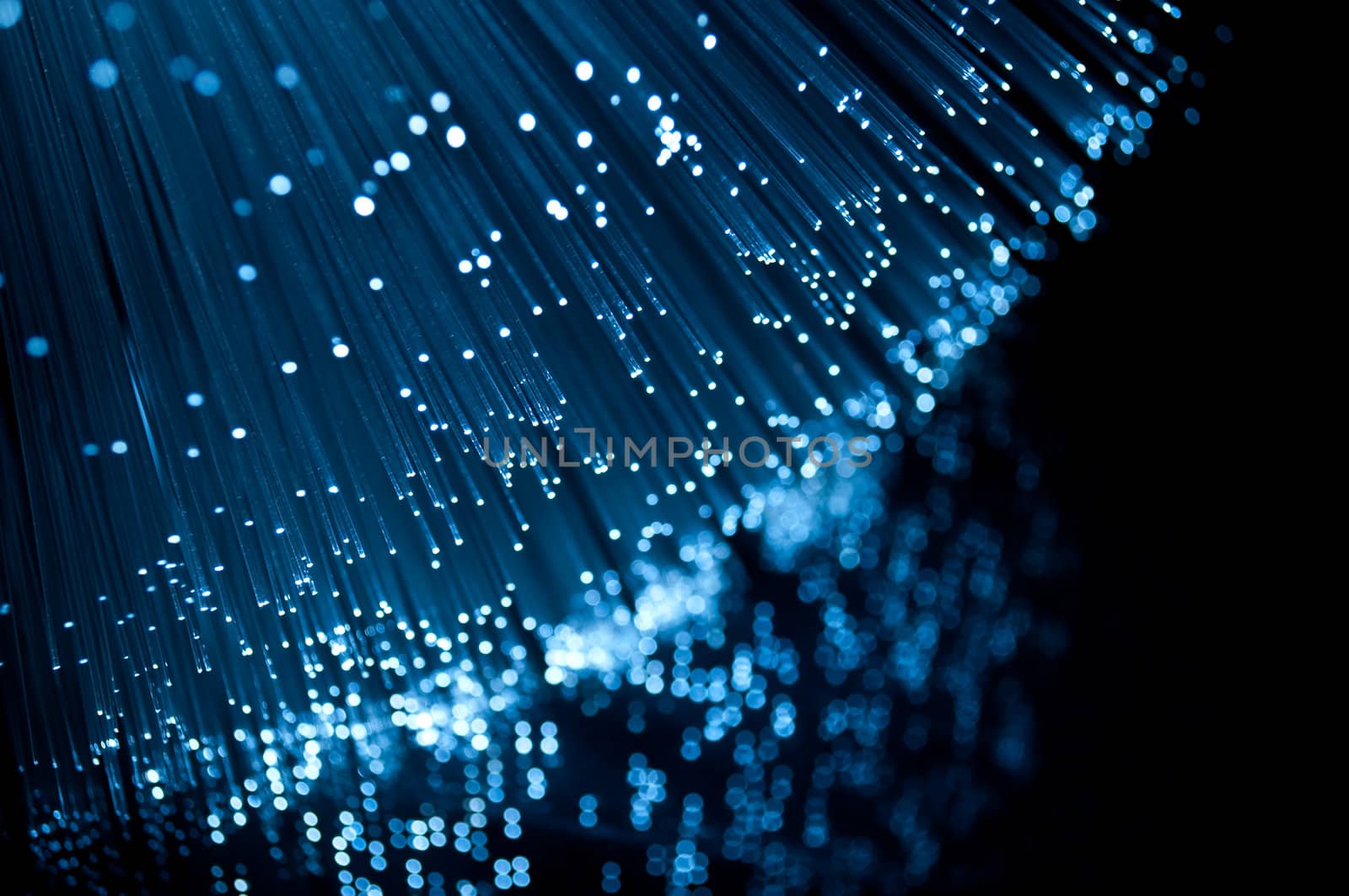 Close up on the ends of many blue illuminated fibre optic light strands against a black background and reflecting into the foreground.