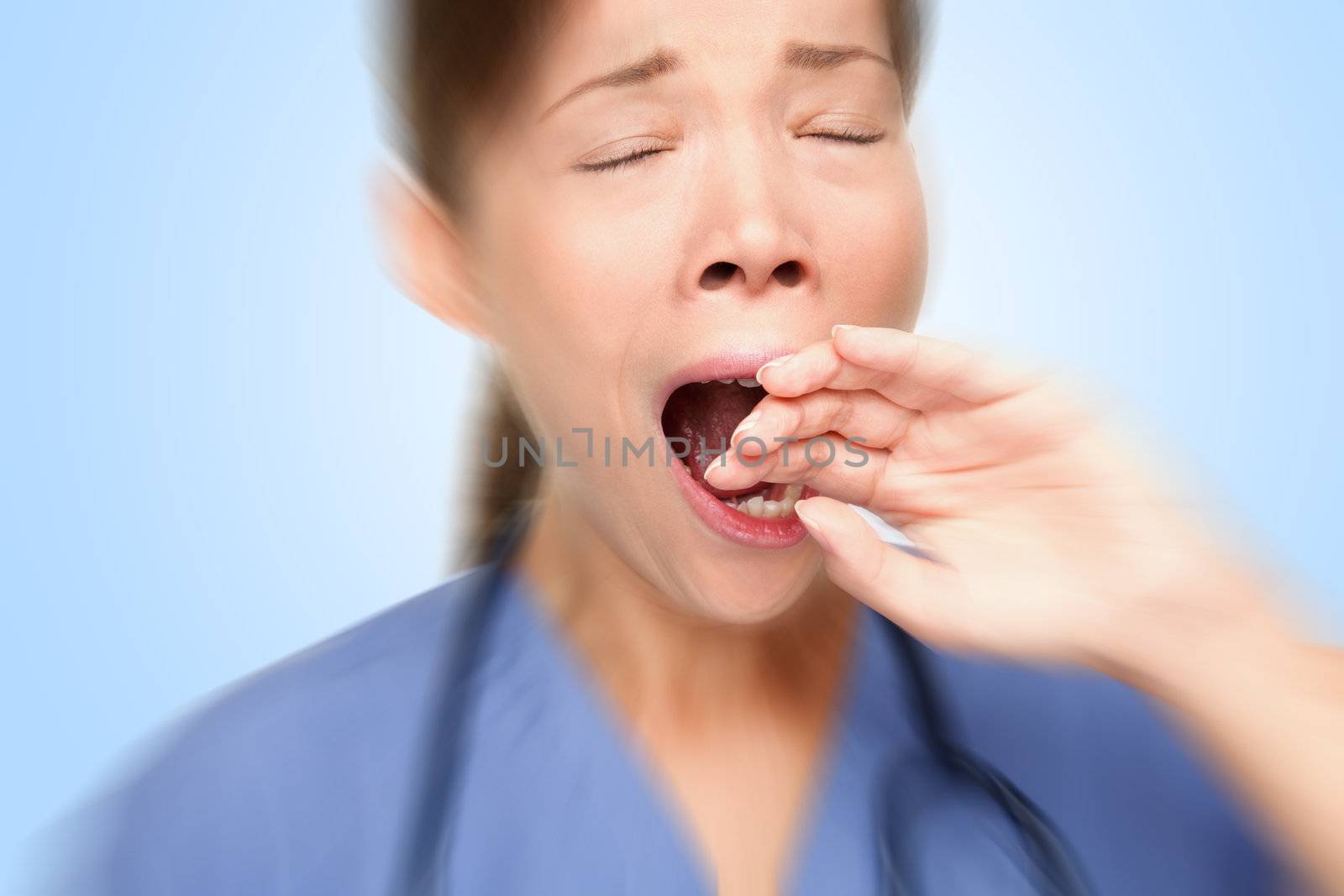 Tired young female nurse / doctor yawning at work. Young Asian / Caucasian woman model. Studio photo.