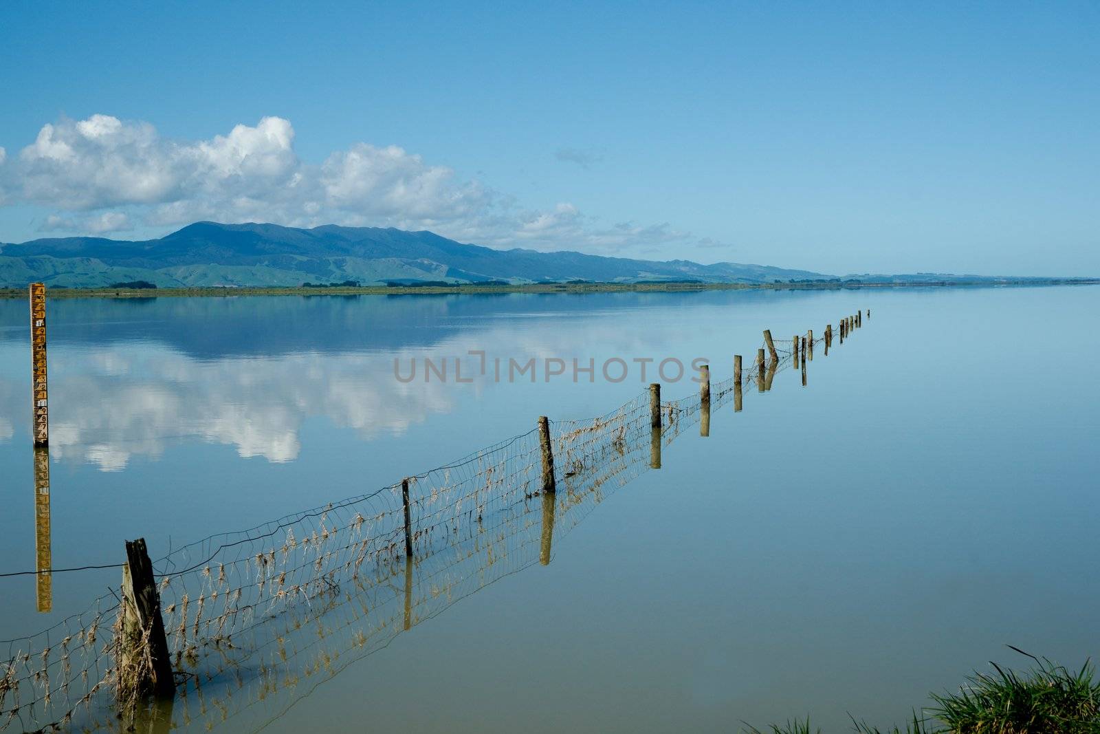 Calm Lake, fence and reflections of distant hills and clouds.