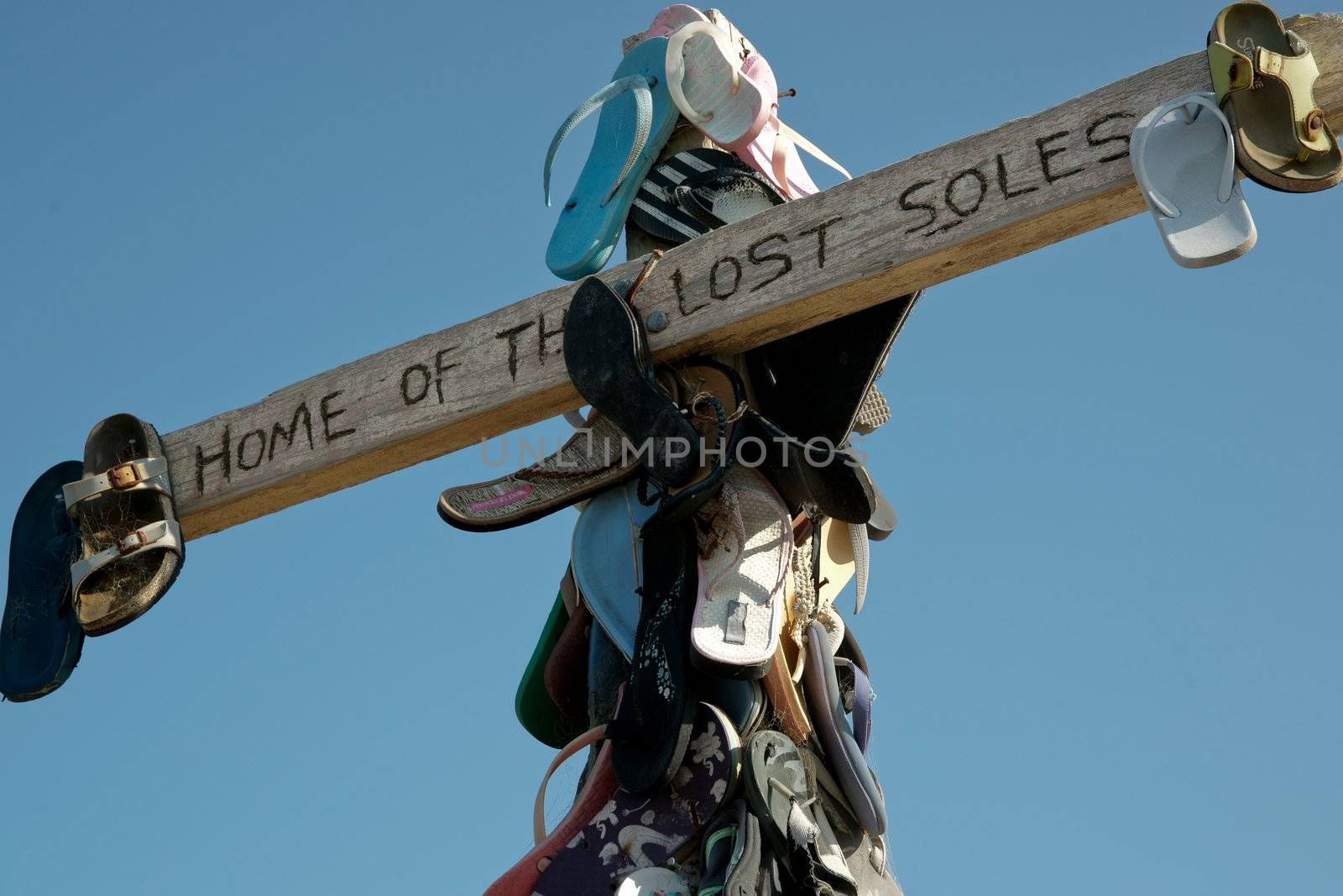 Old beach footwear attached symbolically to a wooden cross on beach.