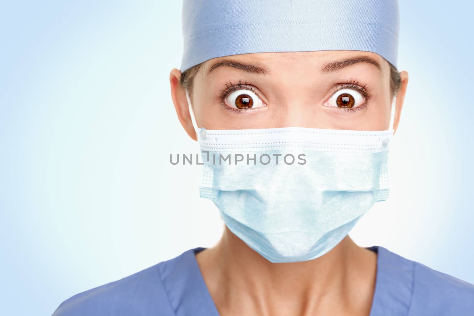 Doctor / surgeon shocked - funny. Woman closeup portrait of young doctor, surgeon or nurse surprised starring with big eyes wearing surgical mask. Asian / Caucasian female model. 