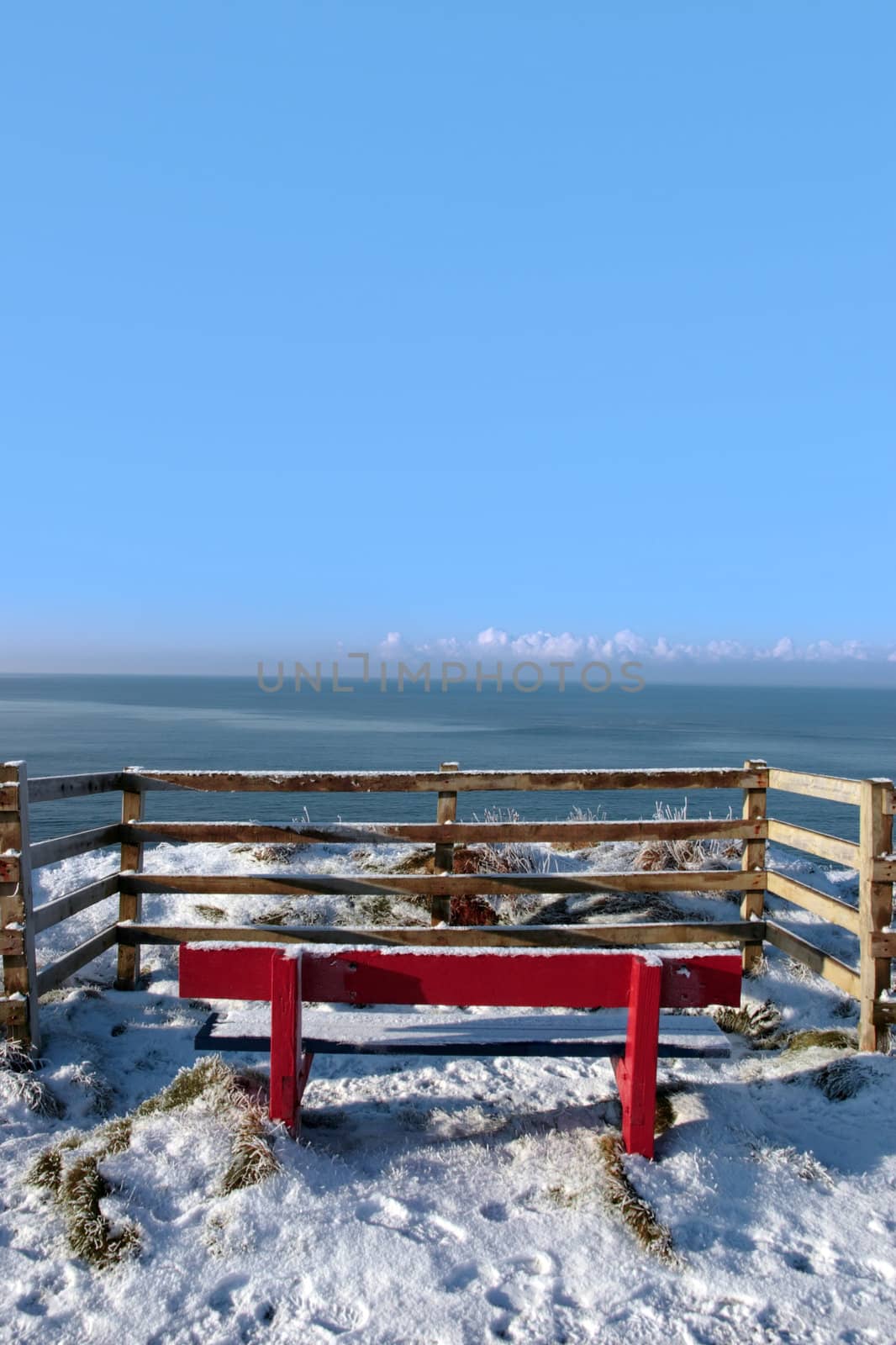 a seasonal snow frosty covered red bench with a sea view and blue cloudy sky background with copy space