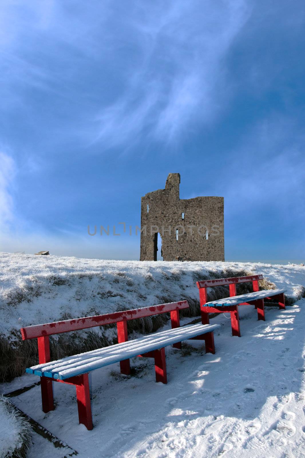 a seasonal snow covered view of atlantic ocean and ballybunion castle with red benches on a frosty snow covered winters day